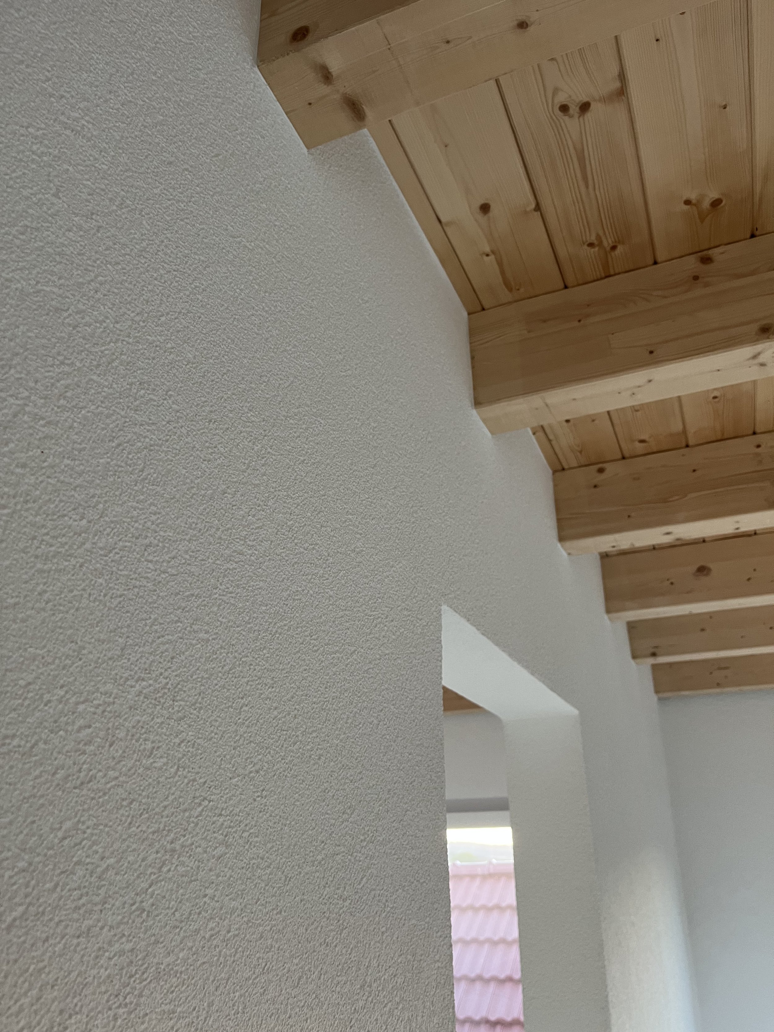 Innenansicht eines Zimmers mit weißen, rauen Wänden und einer Holzdecken mit sichtbaren Holzbalken.