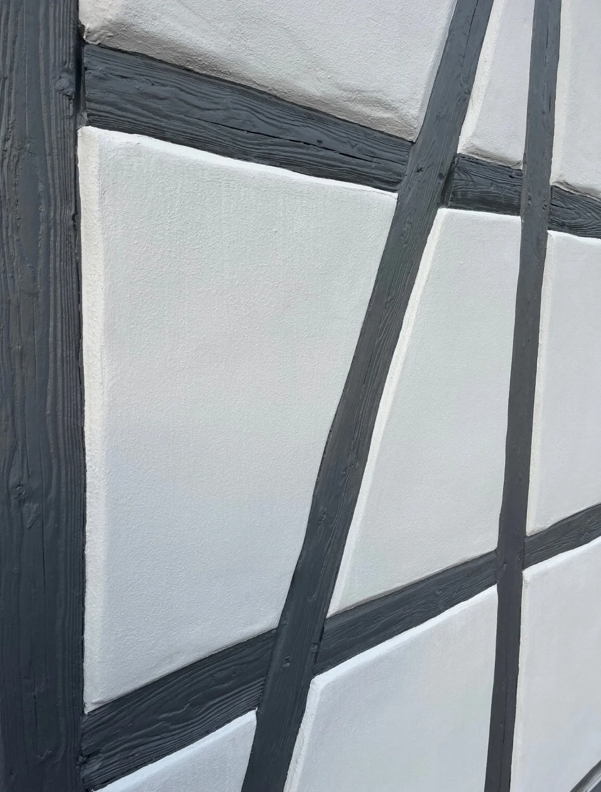 Nahaufnahme einer Wand mit einer modernen, geometrischen Holz- und Putzgestaltung, bestehend aus weißen Putzflächen und schwarzen Holzrahmen.