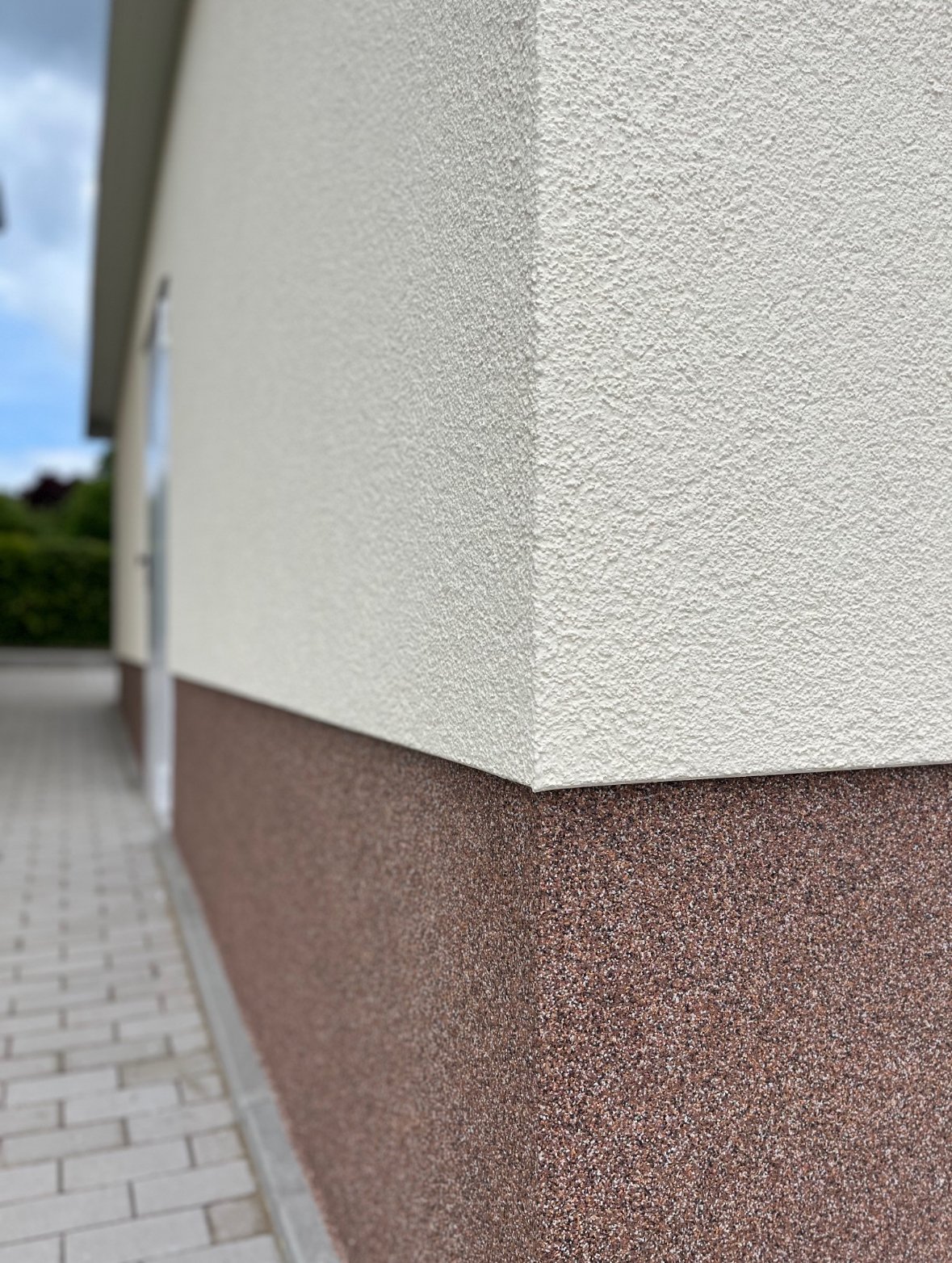 Außenwand eines Gebäudes mit einer zweifarbigen Oberfläche, oben weiß und unten rotbraun, mit Terrasse und Himmel im Hintergrund.