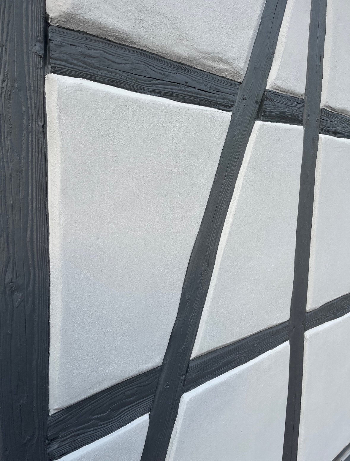 Nahaufnahme einer Wand mit weißen Panelelementen und schwarzen Holzrahmen, die in einem diagonalen und rechteckigen Muster angeordnet sind.