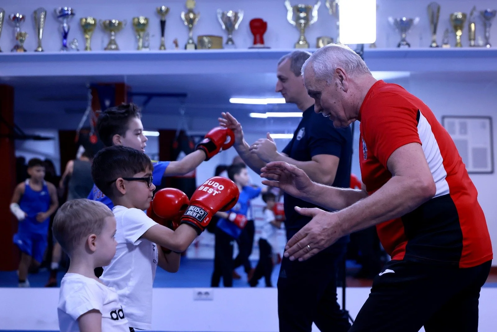 Children practicing boxing in a gym, with trainers guiding them during a training session.