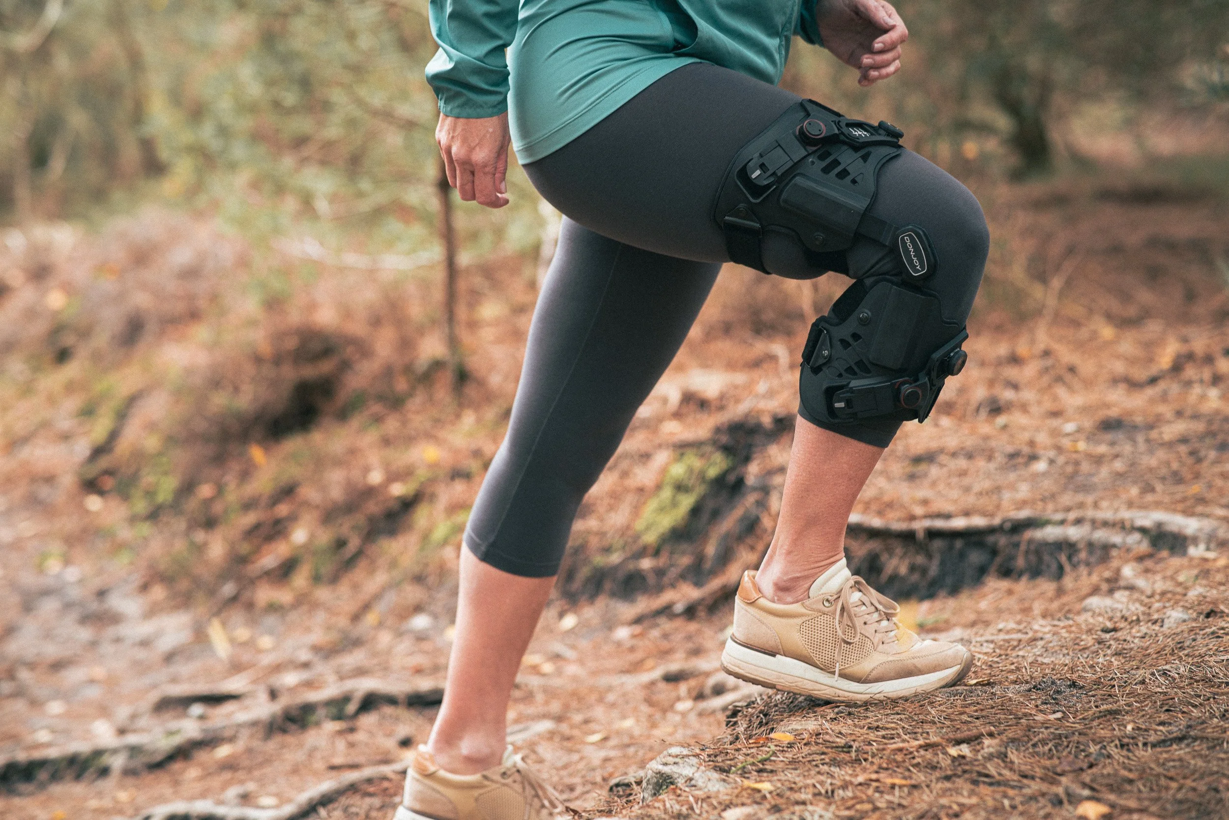 A person wearing a knee brace while hiking outdoors on a trail surrounded by trees and leaves.
