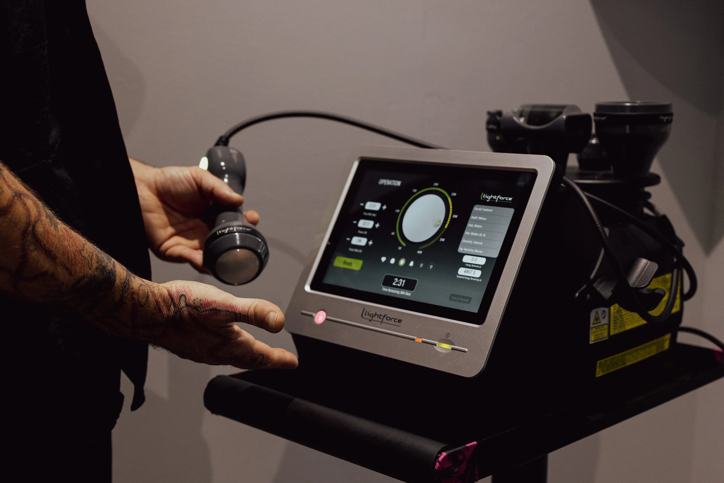 Person holding a Intensity Laser Therapy connected to the digital control panel, on a black rolling stand.