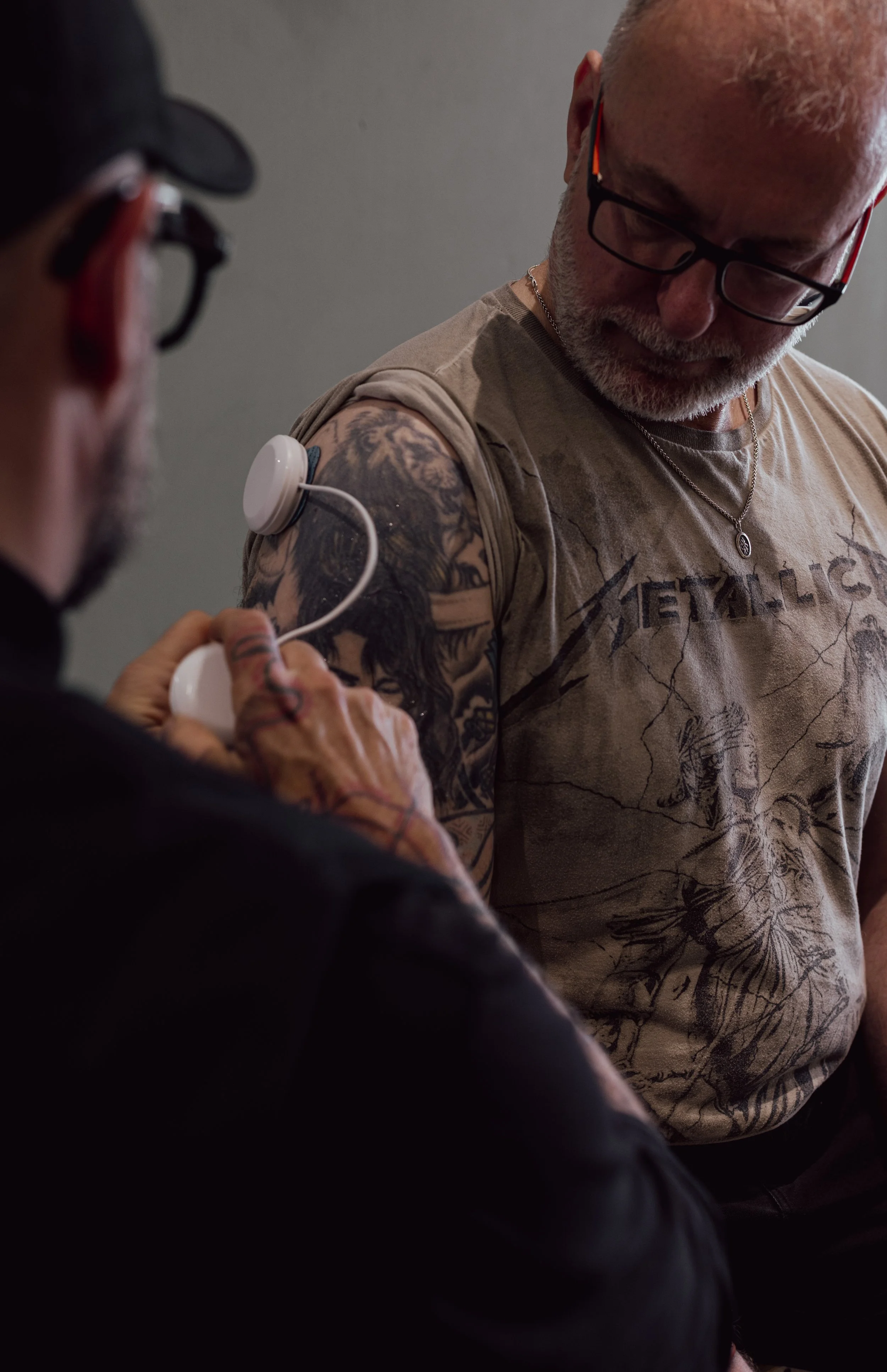 A man receiving neuromuscular electrical stimulation on his biceps, assisted by a physio therapist.