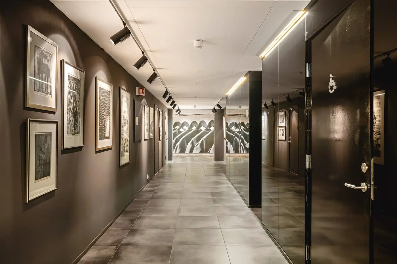 Korridor i et kunstgalleri med bilder hengende på veggene og moderne belysning.