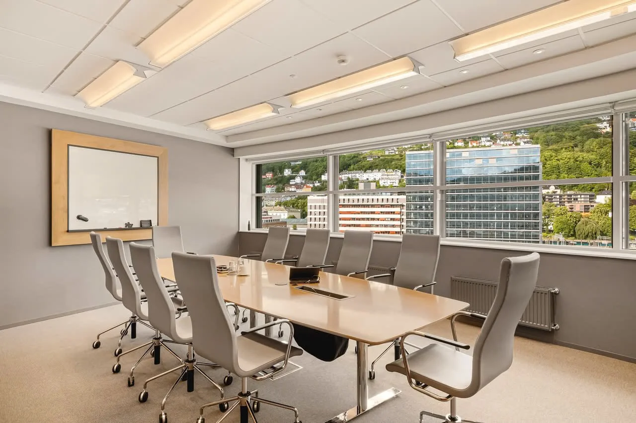 Konferanserom med langbord og stoler, store vinduer med utsikt over byen.