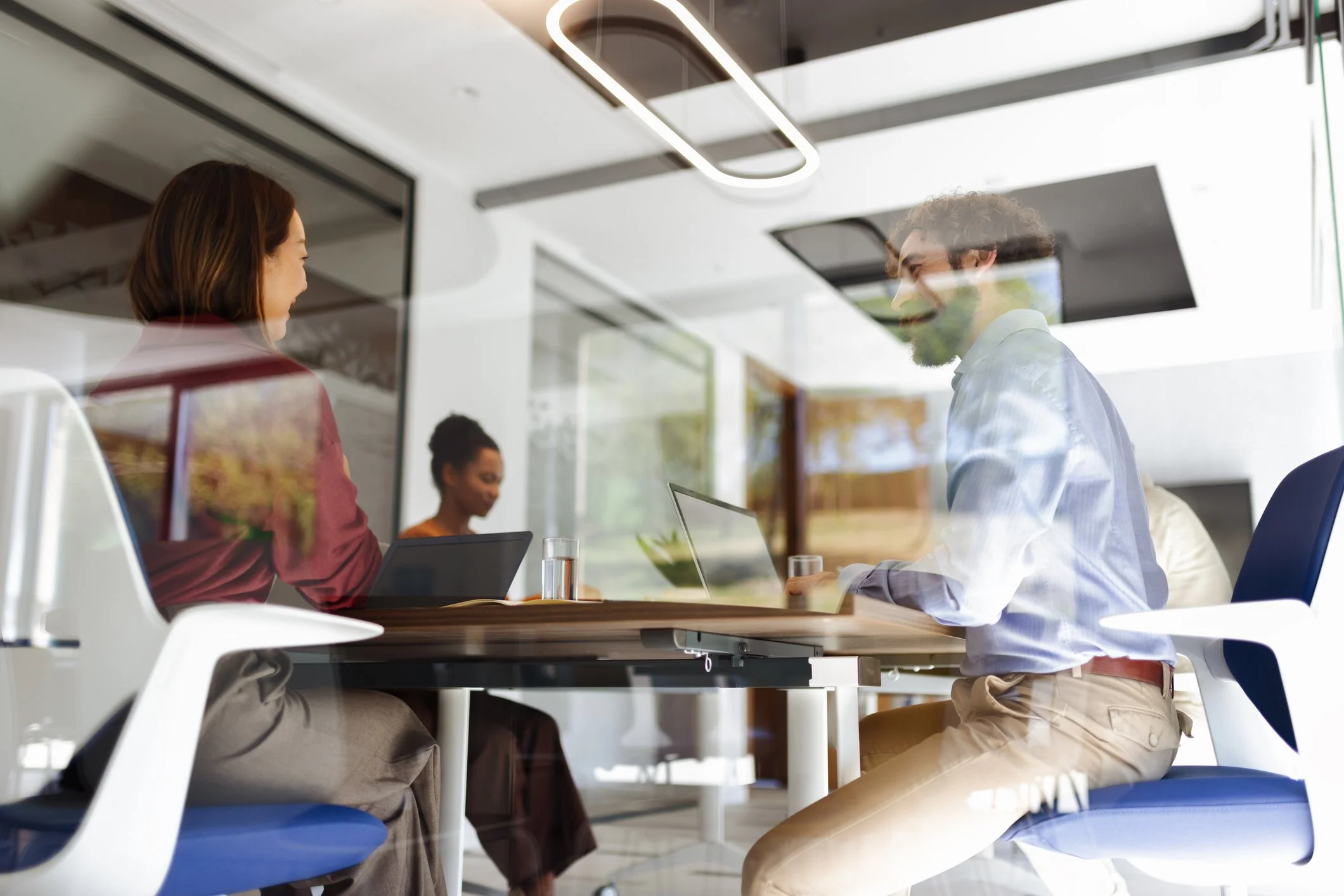 To personer i et konferanserom som har et møte, sett gjennom et glass med refleksjoner.