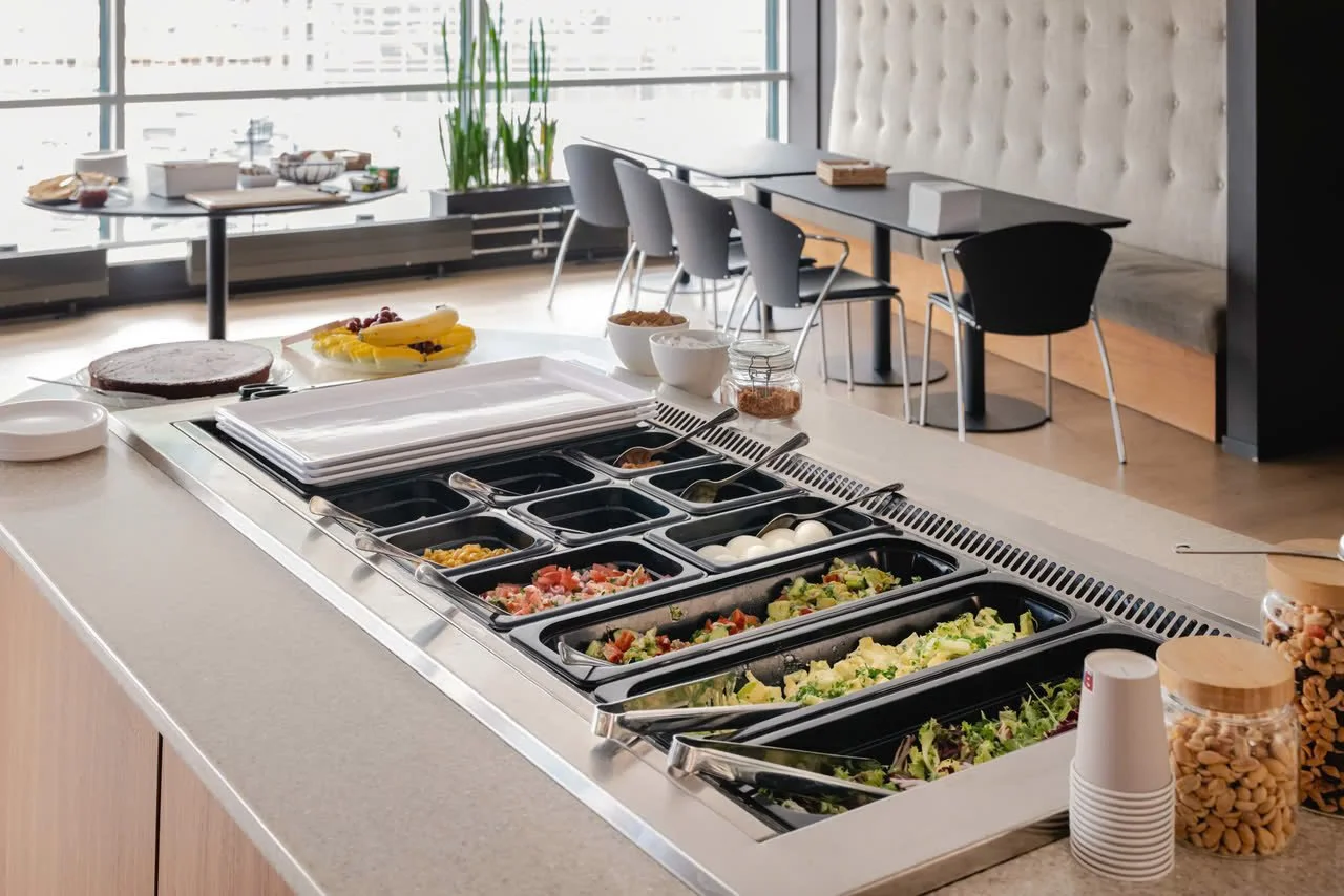 Buffet med forskjellige salater, kokte egg, frukt, kaker og toppings i en moderne spisesal.