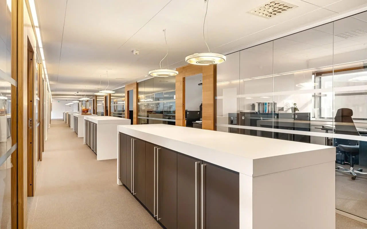 Tom arbeidsplass med hvite og grå skap, glassvegger og moderne lysarmaturer.
