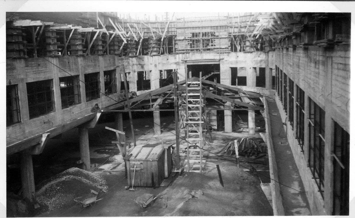 Bygningsarbeid under oppføring med stillaser, stiger og byggeutstyr i en innendørs byggeplass.