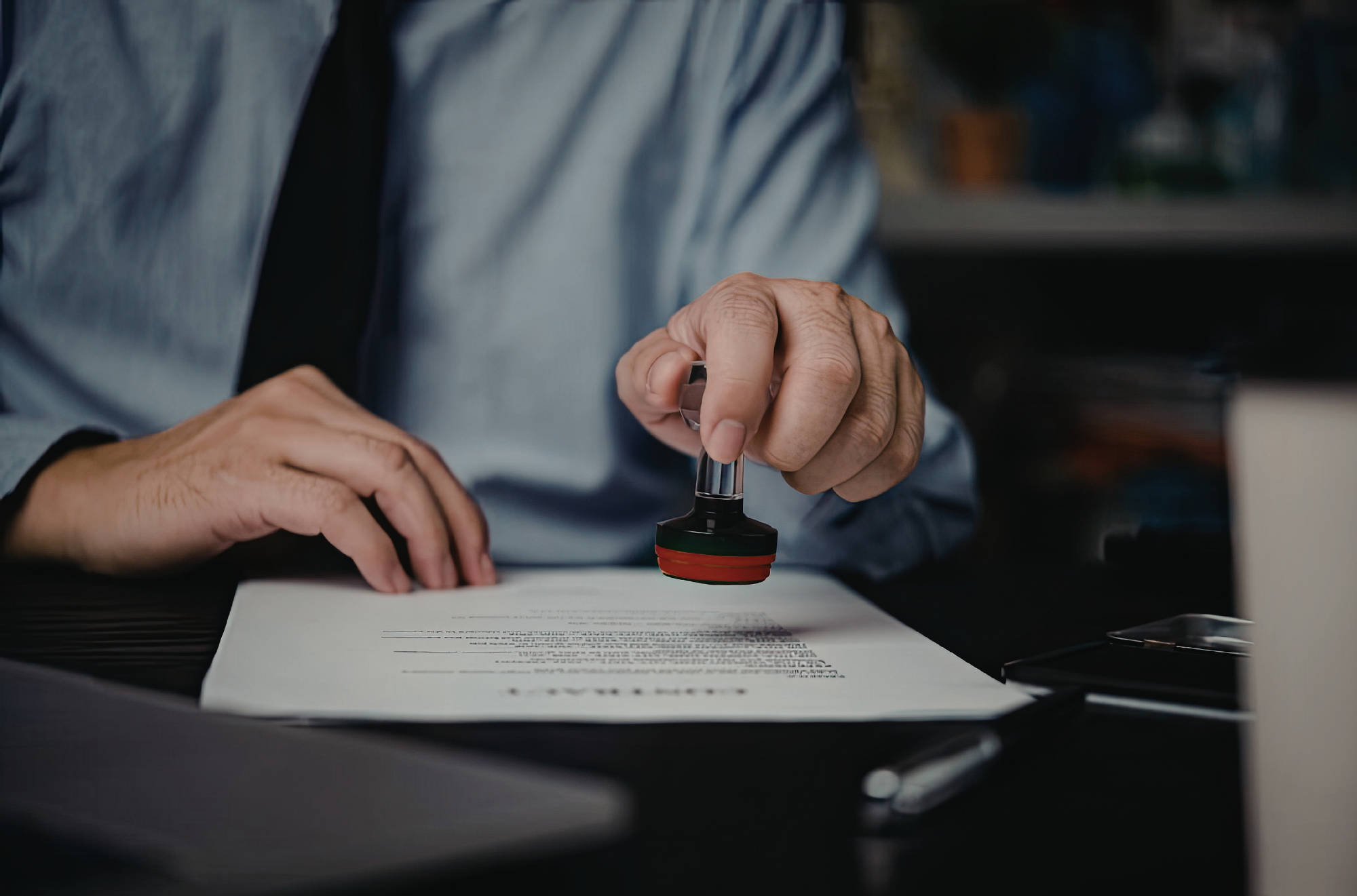 A person in a blue shirt is stamping a document with a red and black rubber stamp.