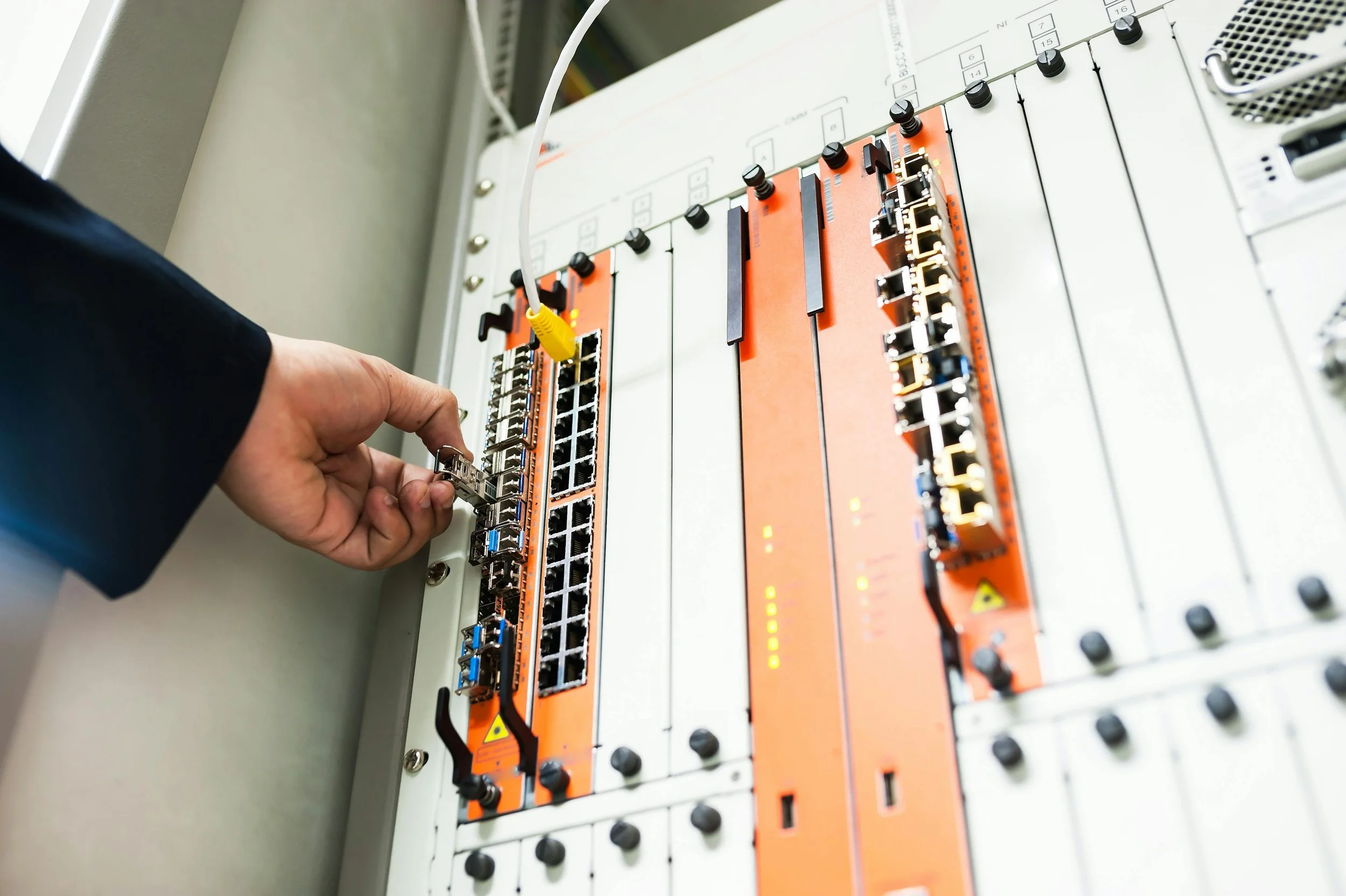 A person connecting or disconnecting Ethernet cables to a networking device inside a server or networking rack.