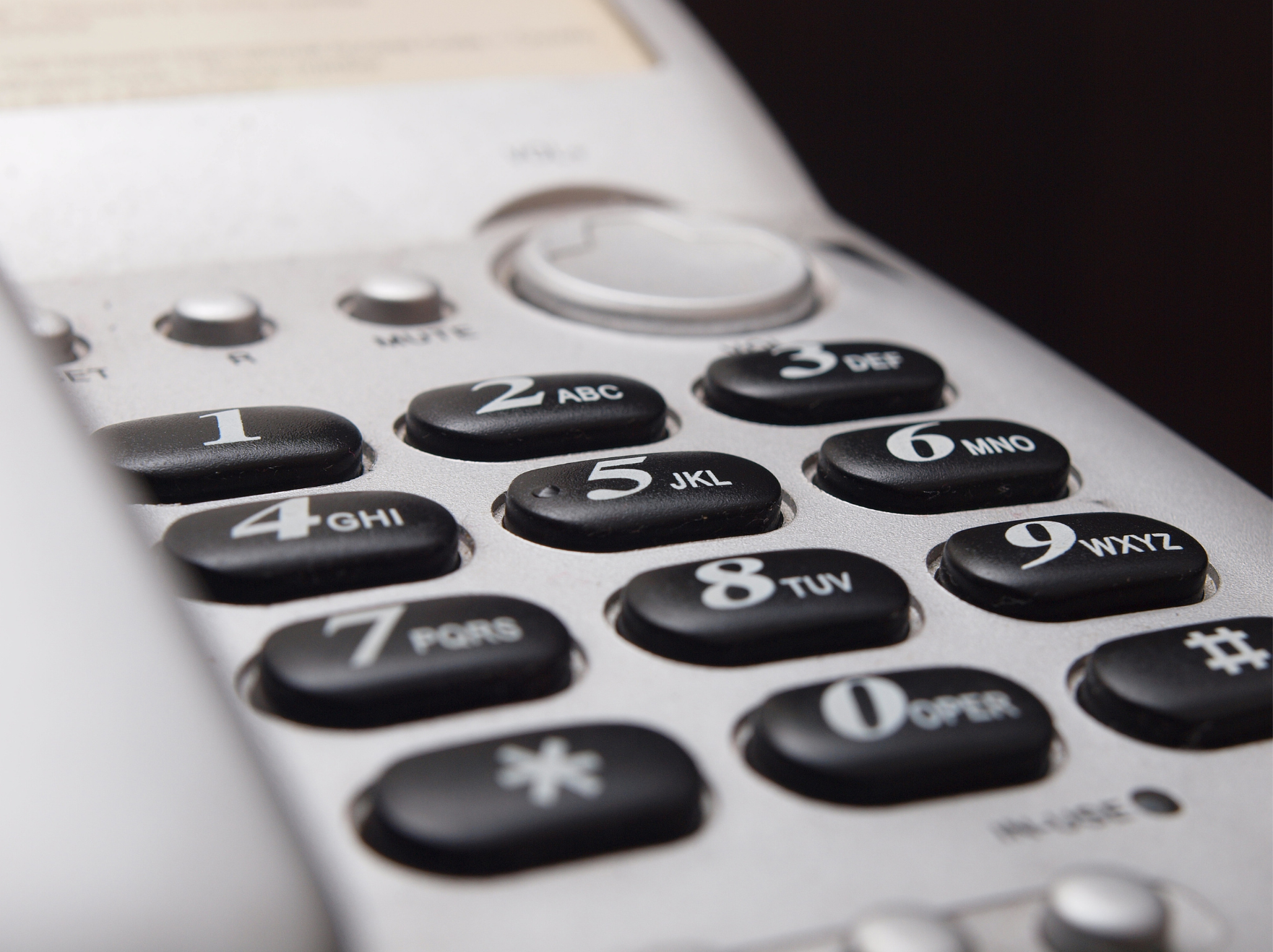Close-up of a telephone keypad with black buttons and white numbers and letters, part of a white telephone.
