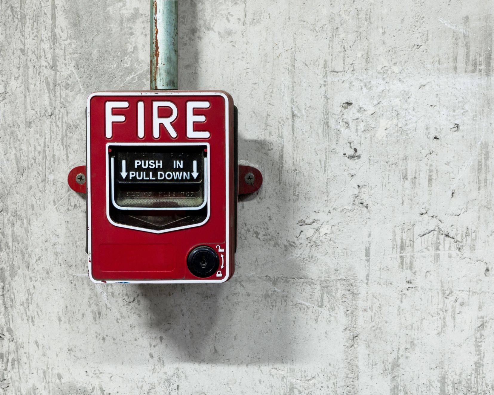 A red fire alarm pull station mounted on a textured light gray wall.