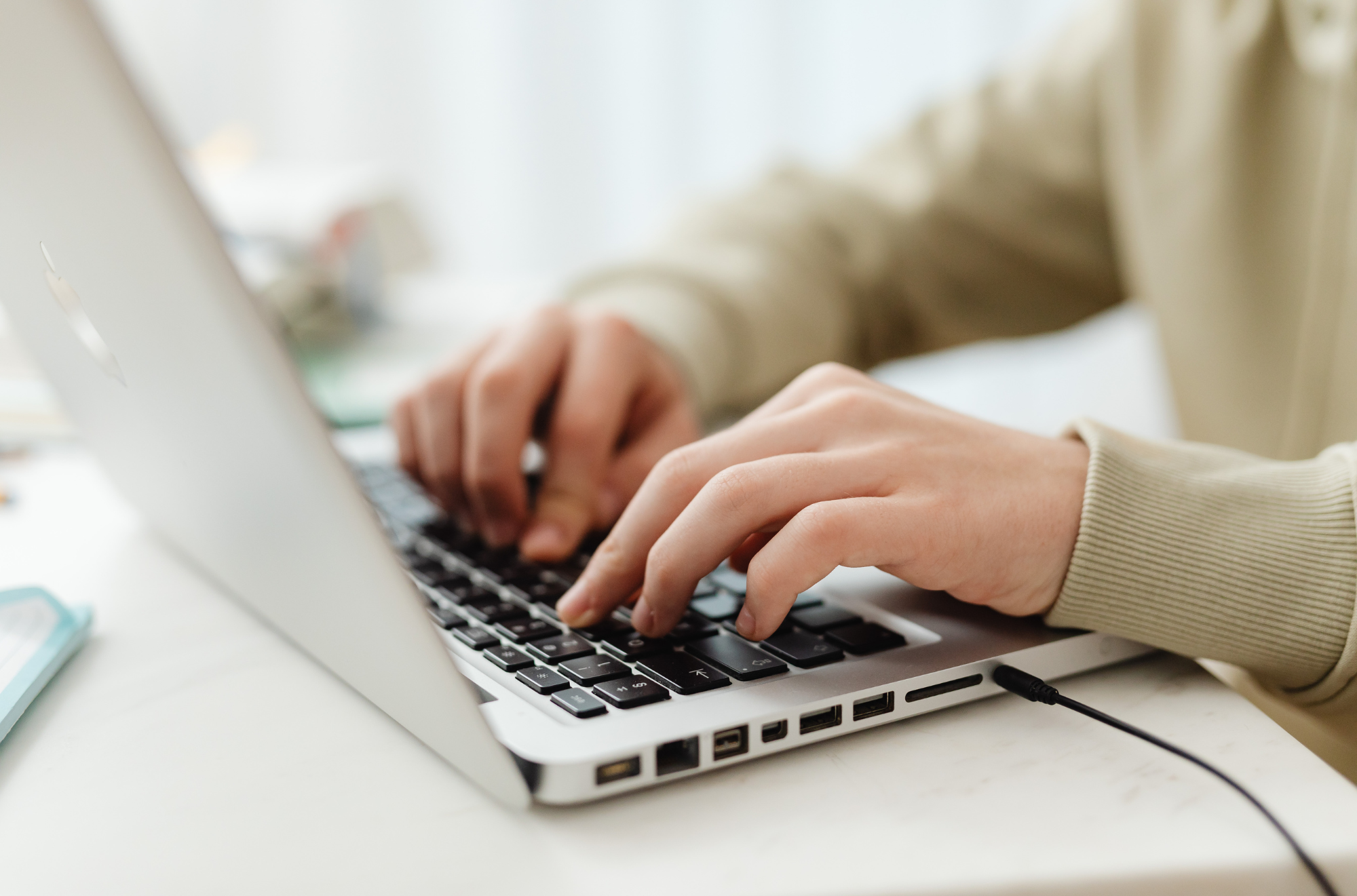 Close-up of a person's hands typing on a laptop keyboard on a white desk.