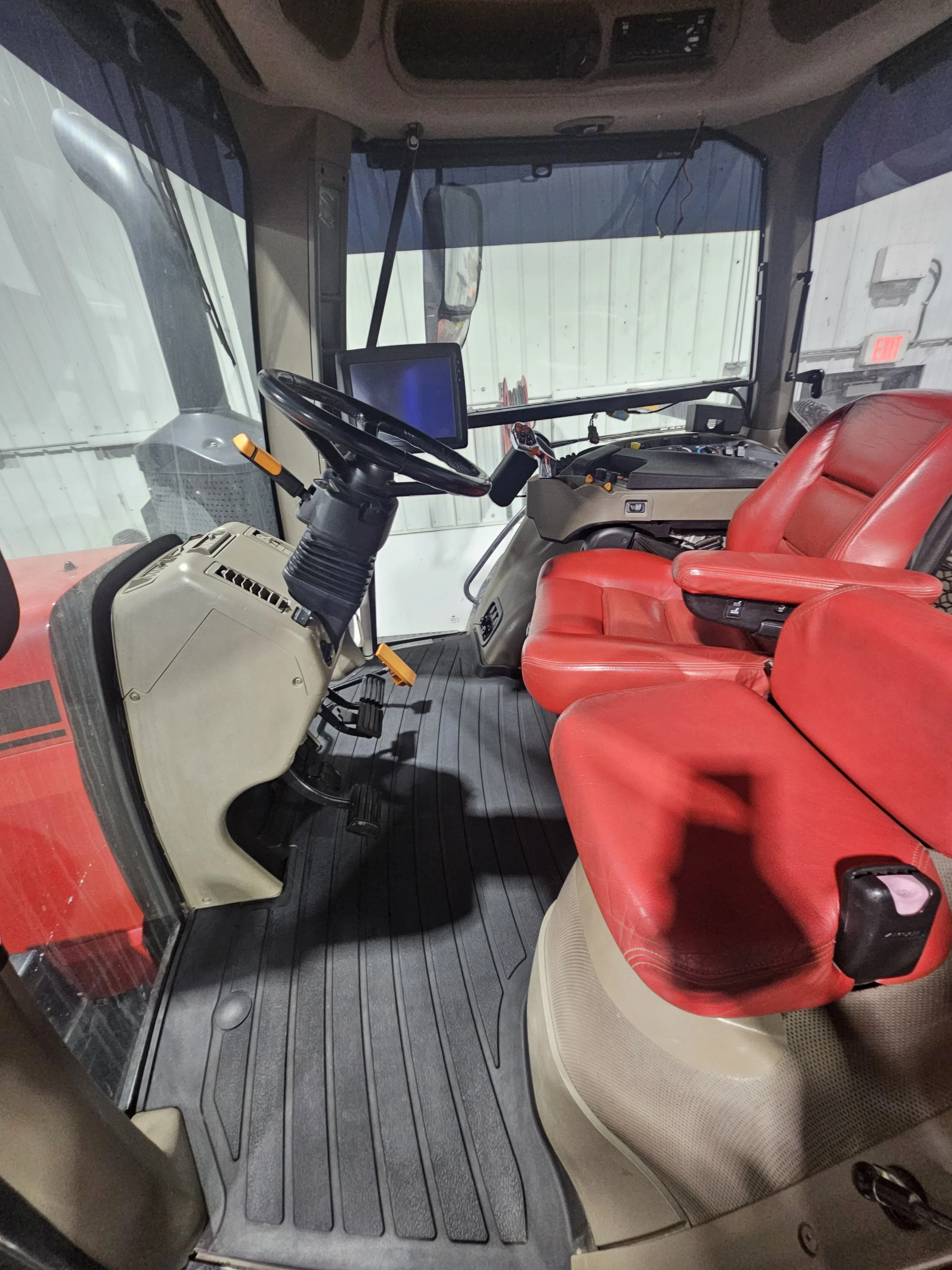 Interior of a tractor cab with red seating, steering wheel, dashboard, and a digital display screen.