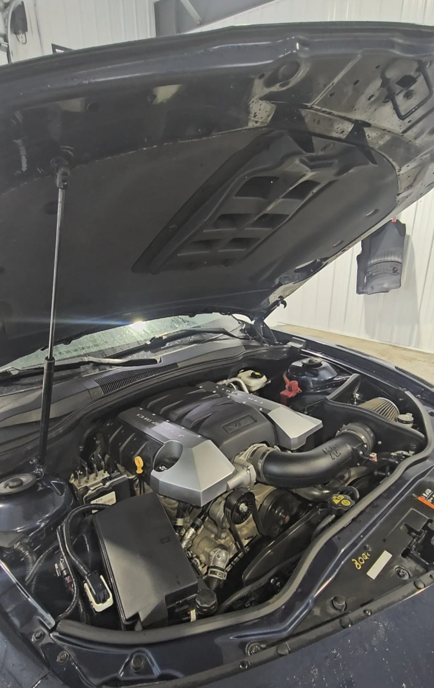 Car engine bay with hood open, showing engine, air filter, and other engine components.
