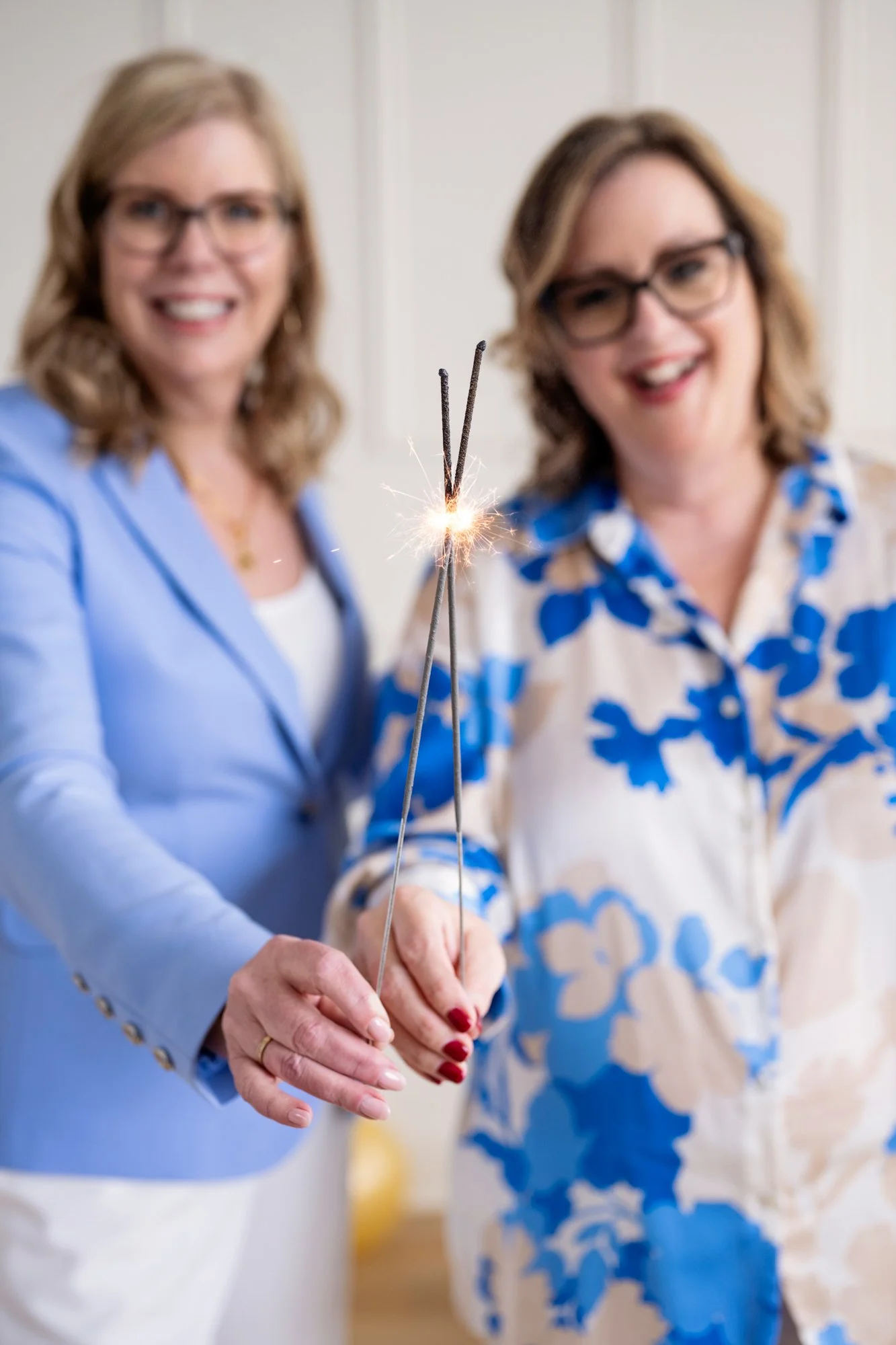 Deux femmes souriantes tiennent des chandelles de fête allumées, en arrière-plan.