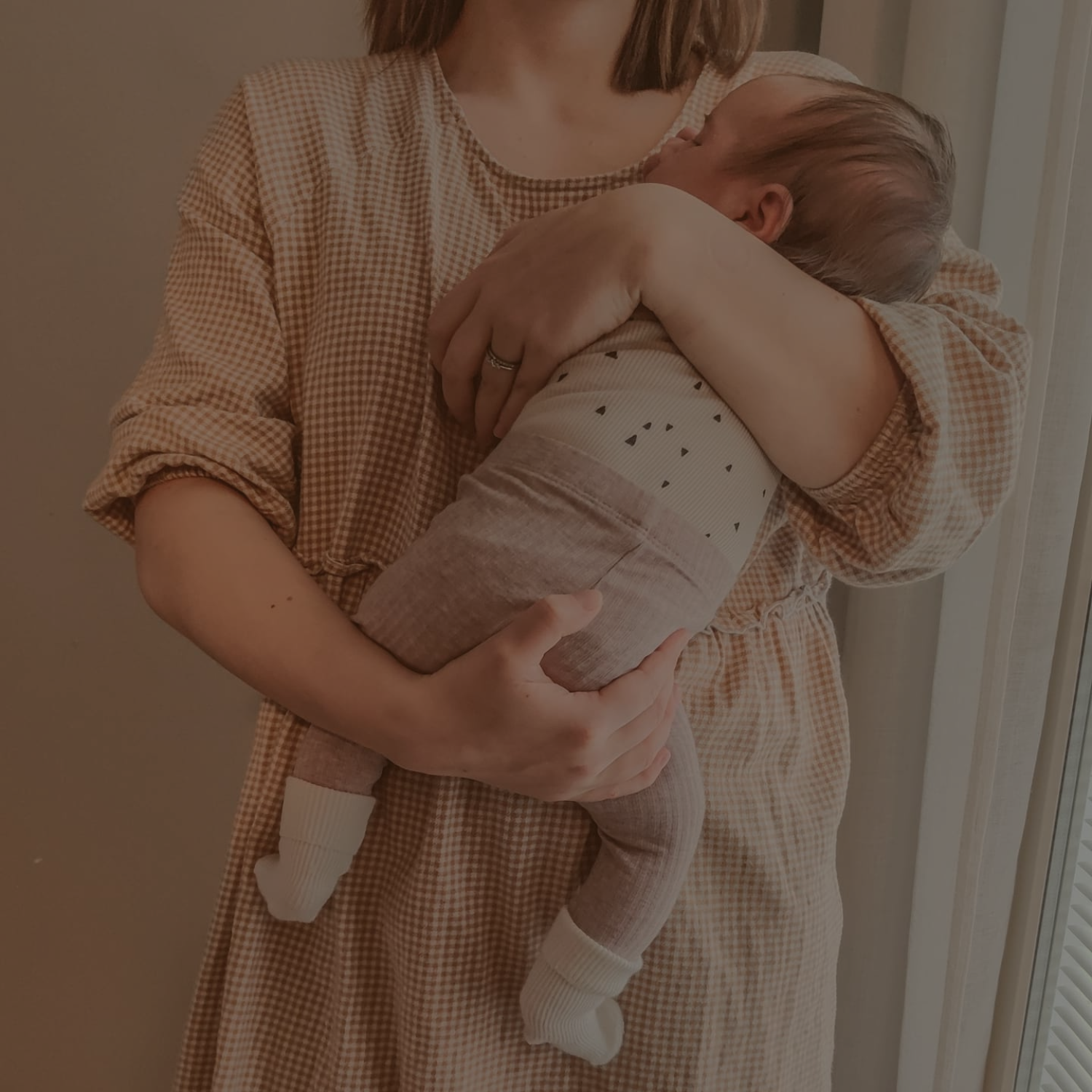 A woman holding a young child close, standing indoors near a window.