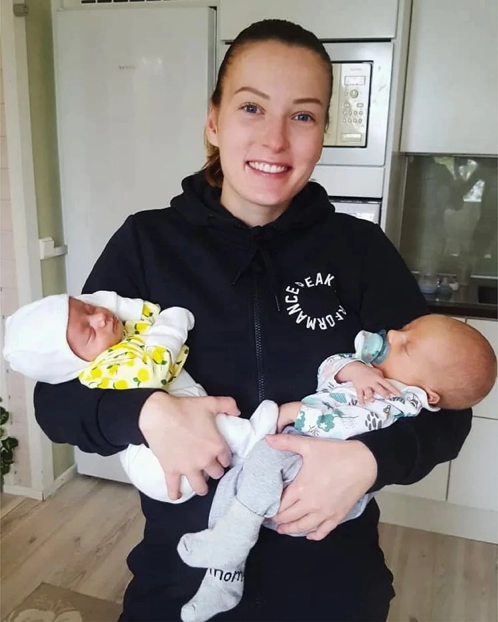 Nuori nainen pitää kahta pientä vastasyntynyttä lasta sylissään.