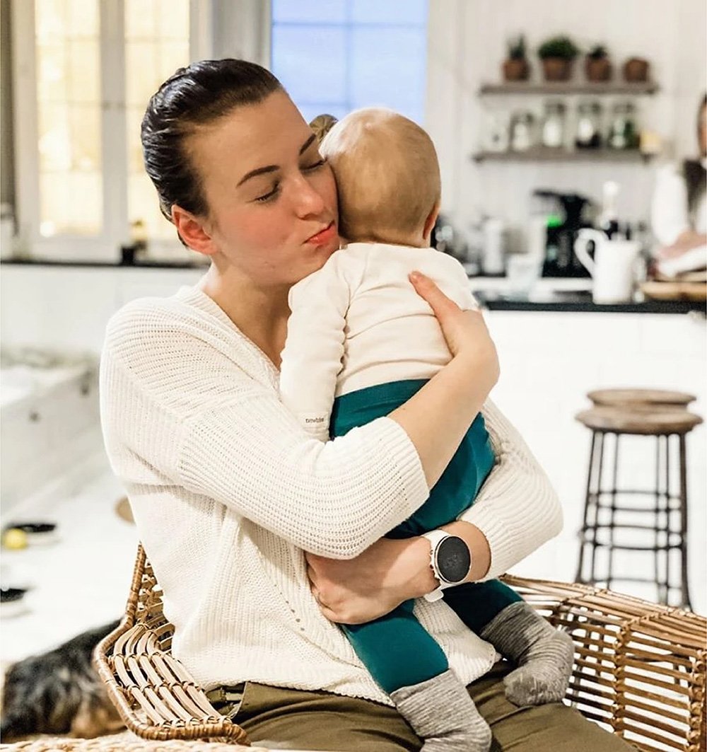 Nainen halaa vauvaa sylissään keittiössä.