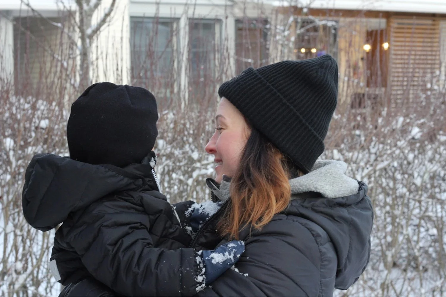 Nainen ja lapsi hymyilevät talvisessa eteläisessä maisemassa, taustalla puita ja rakennuksia.