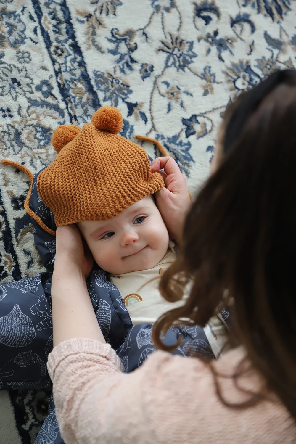 Lapsi makaa sängyllä, päässä oranssi pipo.  Aikuinen katsoo lasta ja koskettaa pipoa.