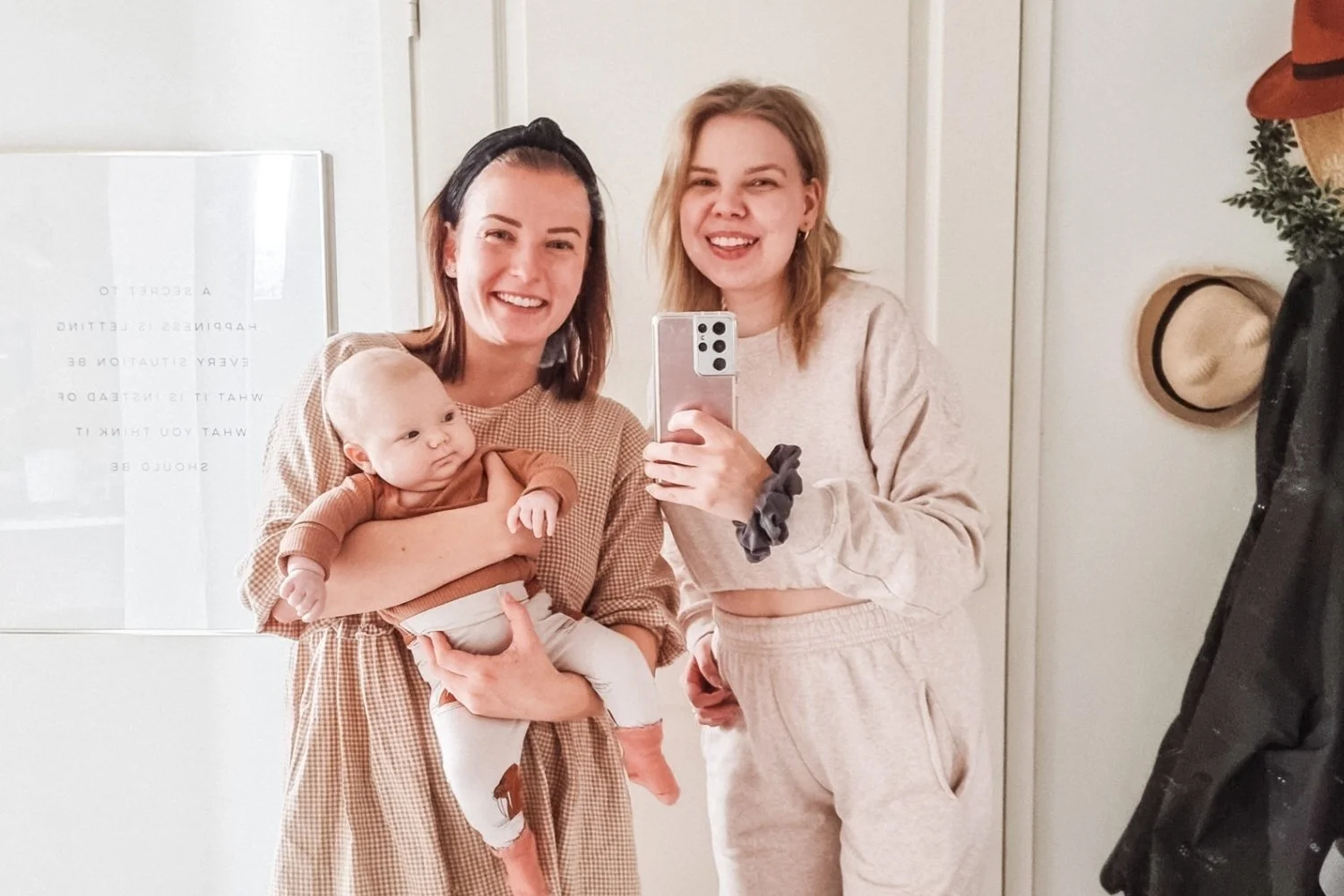 Kaksi naista ja vauva hymyilevät otettaessa selfieä peilistä. Naiset nauttivat ja hymyilevät, vauva katsoo kiinnostuneena.