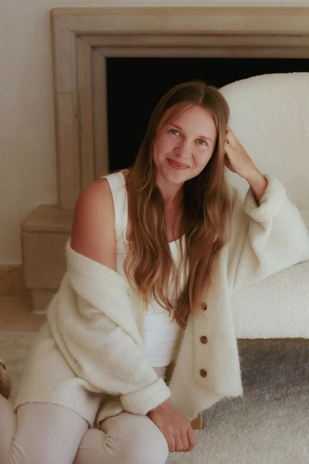 Nainen istuu lattialla, hymyilee ja katsoo kameraan.