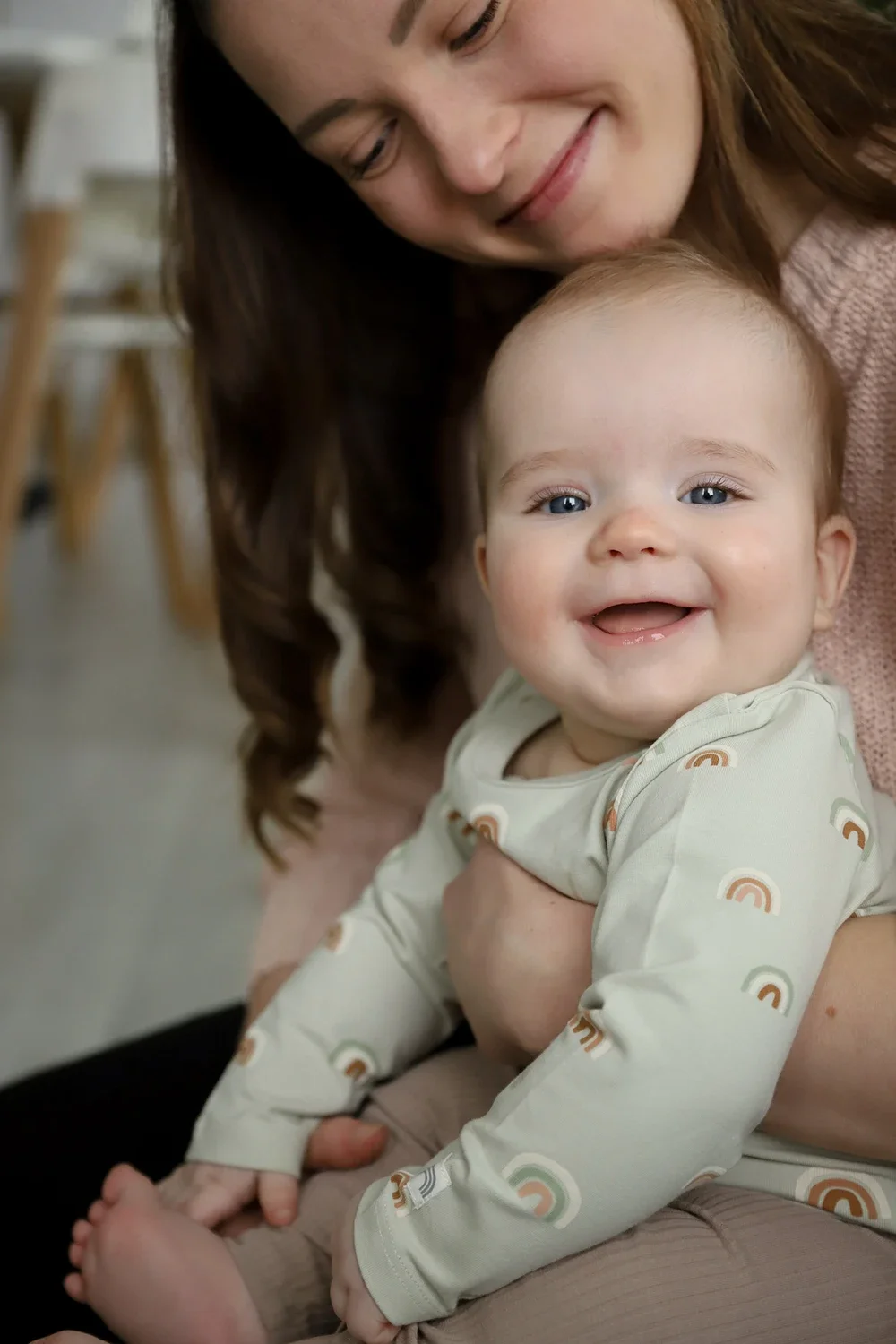 Hymyilevä vauva ja naisen vierellä, sisätiloissa.