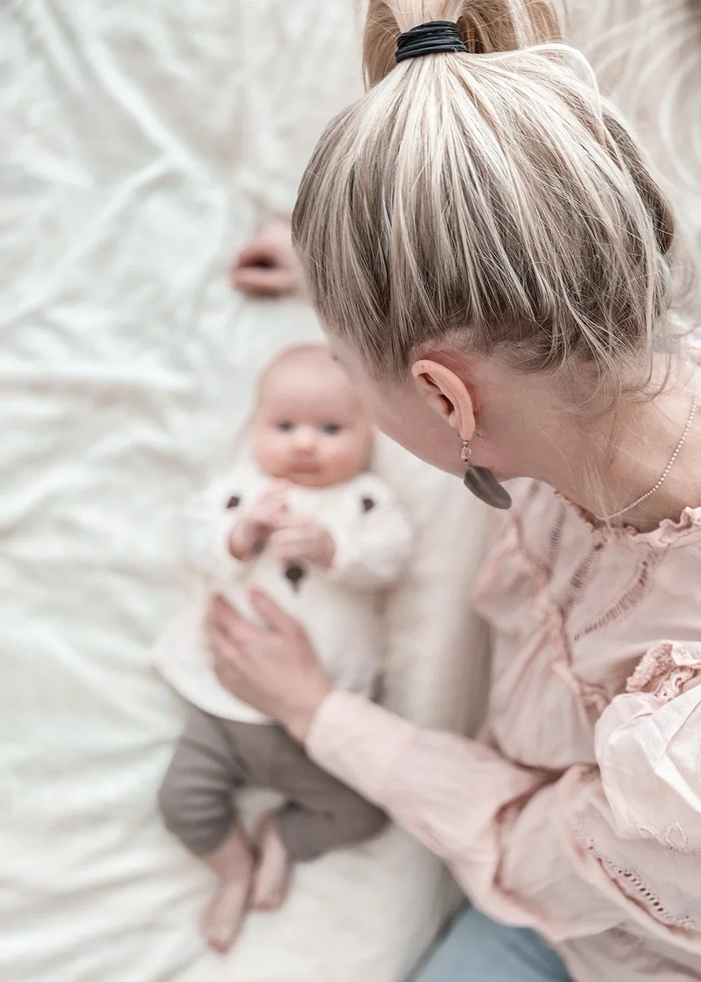 Nainen katsoo pientä lasta, joka on makuulla pehmeällä, vaalealla alustalla.