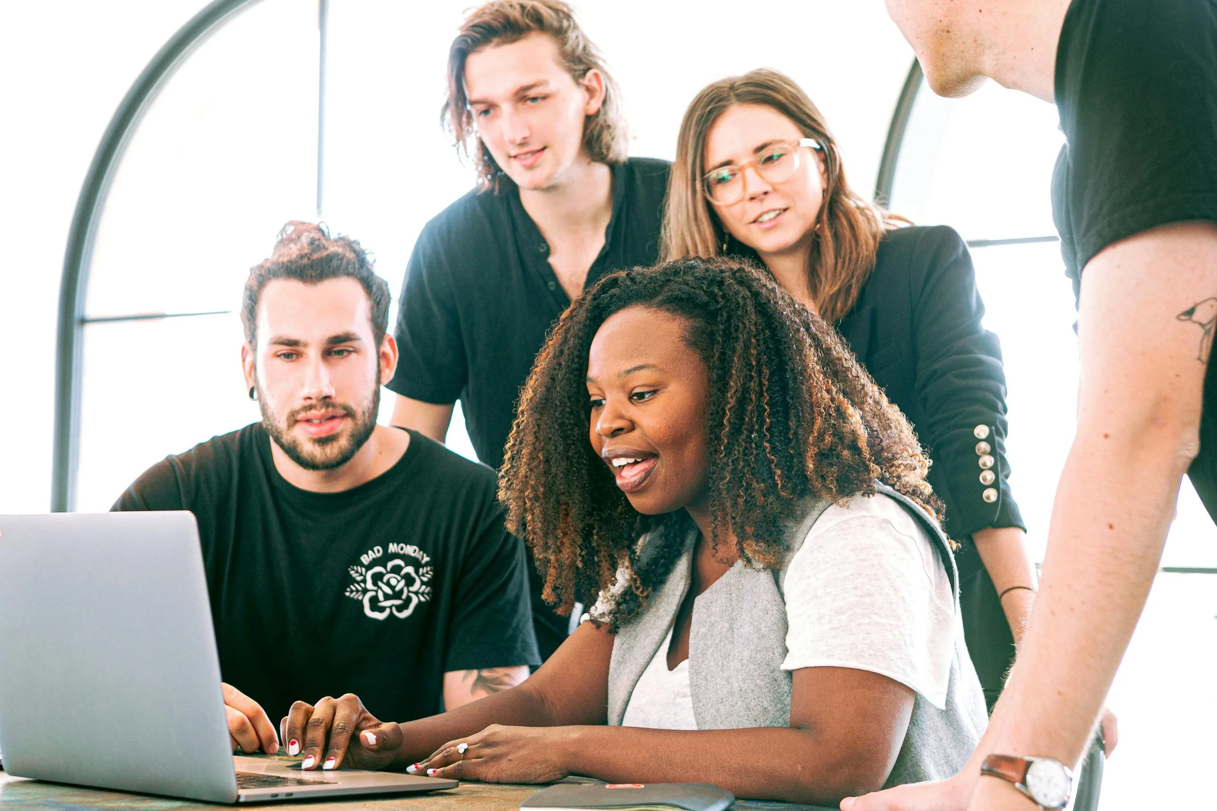 Five young adults gathered around a laptop, looking at the screen and discussing.