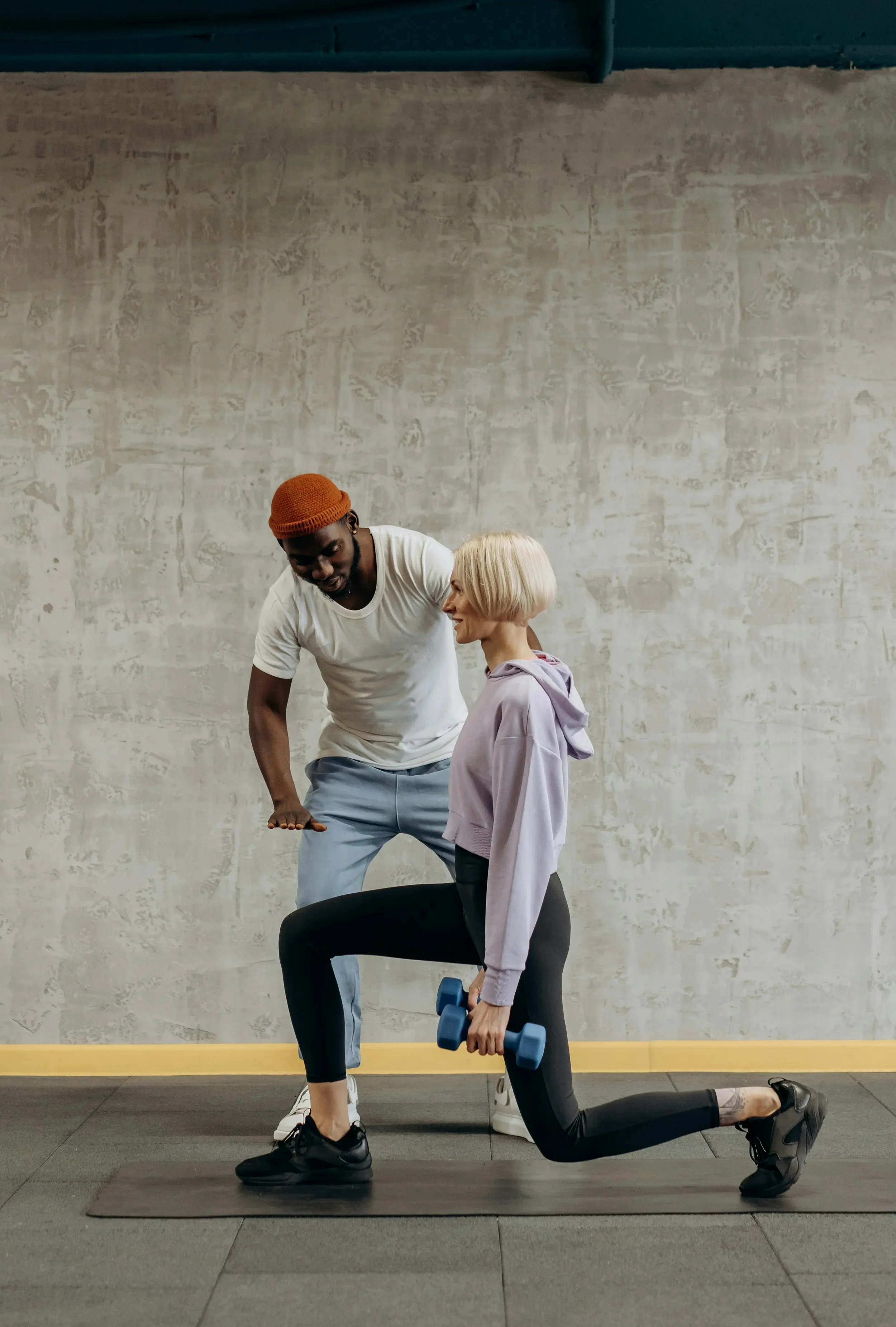 Une femme fait des exercices de musculation avec un haltère sous la supervision d'un entraîneur dans une salle de sport