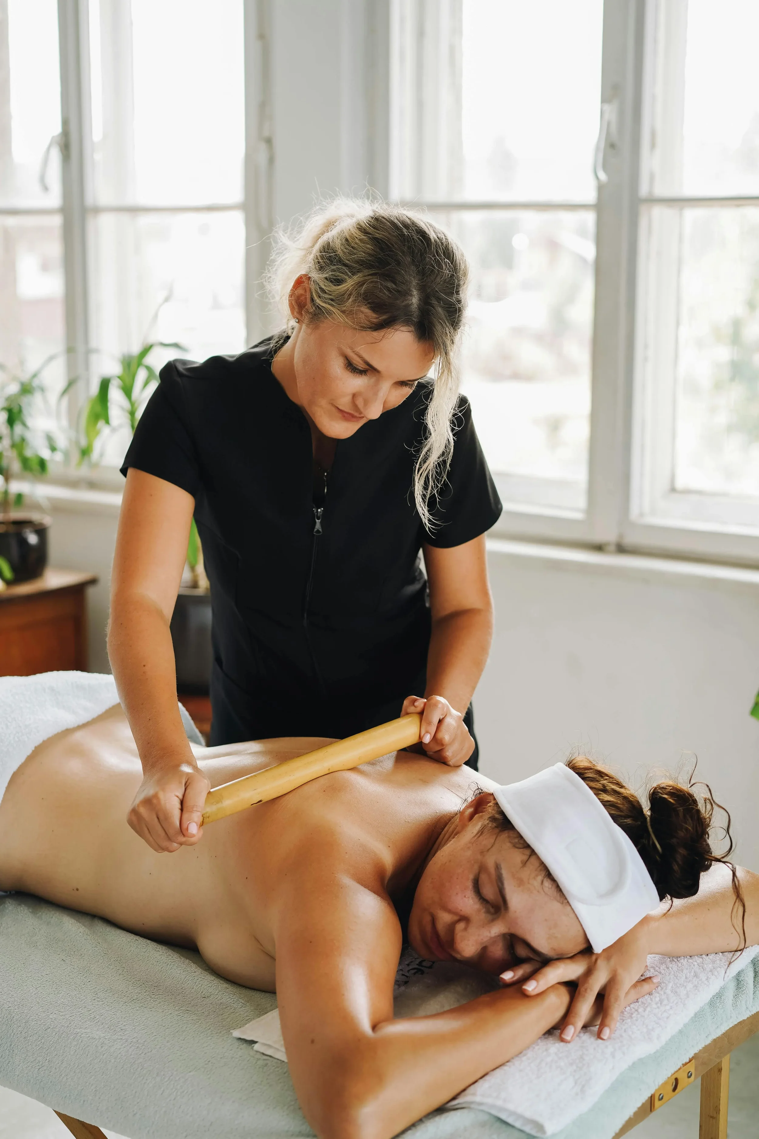 Une femme reçoit un massage avec un bâton en bois par une thérapeute  Ayurveda et médecine asiatique dans un environnement lumineux et spacieux.