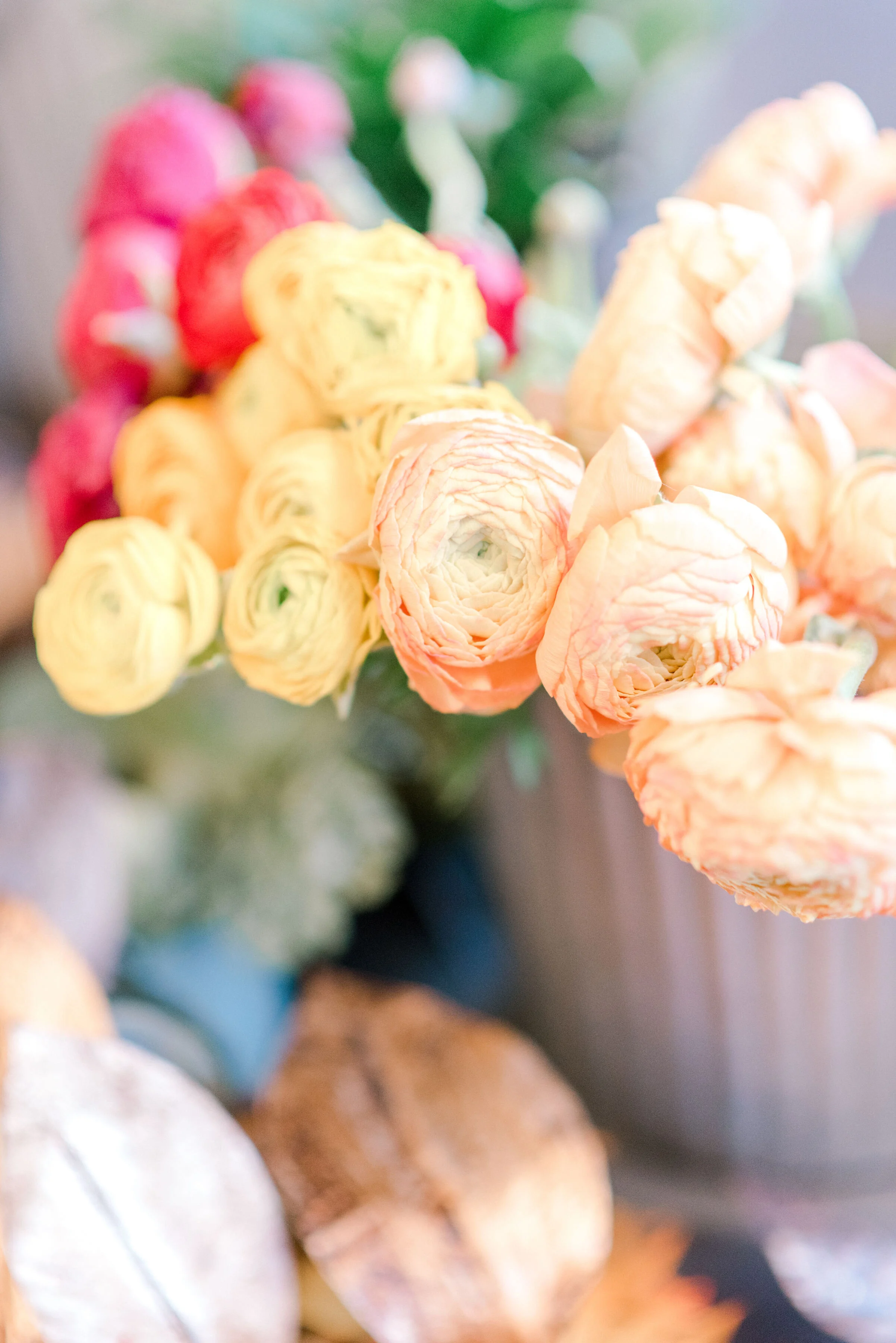 Close-up of a bouquet of peach, cream, and pink ranunculus flowers with green leaves.