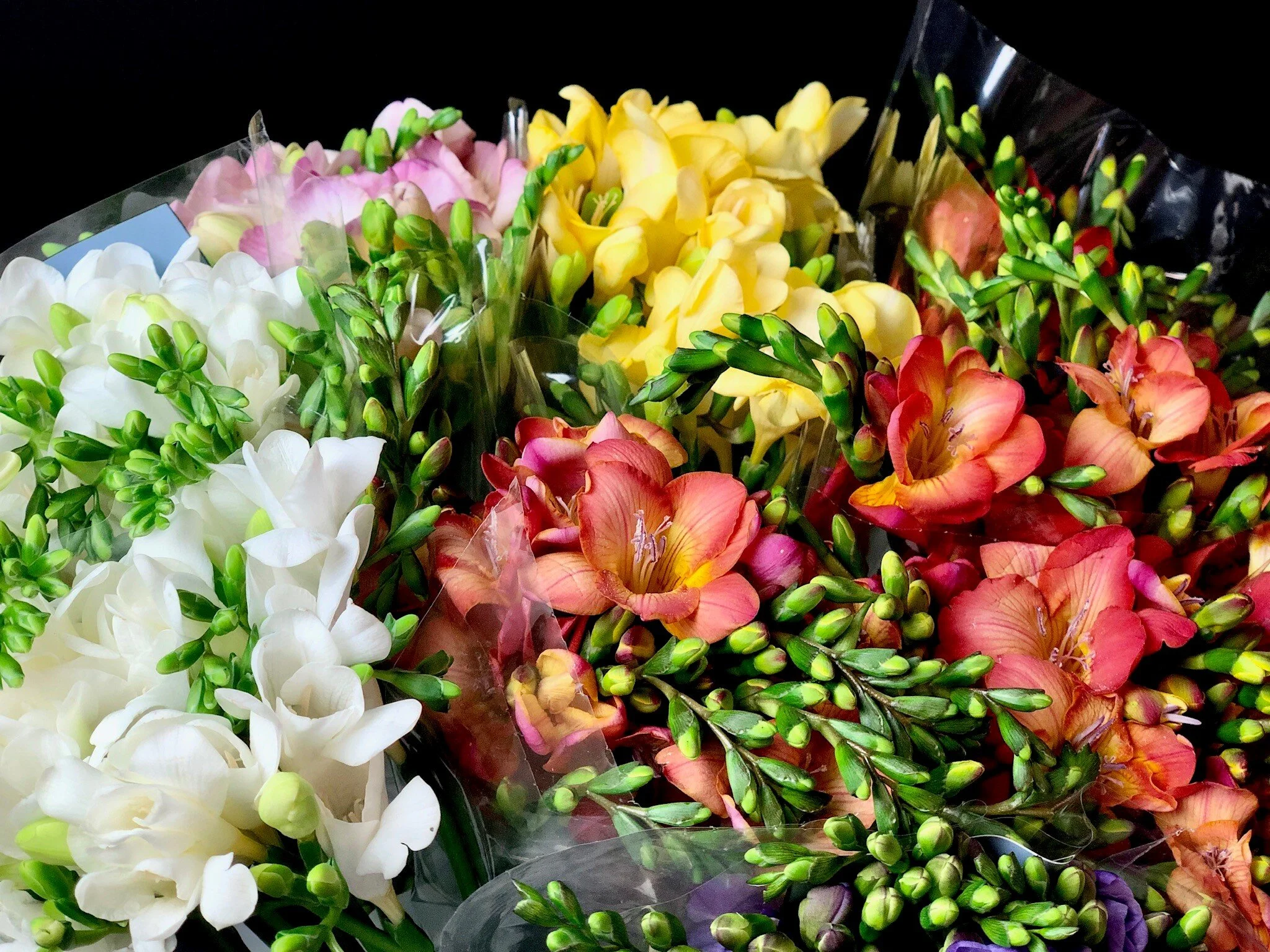 Colorful bouquets of various flowers including white, pink, yellow, and orange blossoms with green foliage, wrapped in transparent plastic.