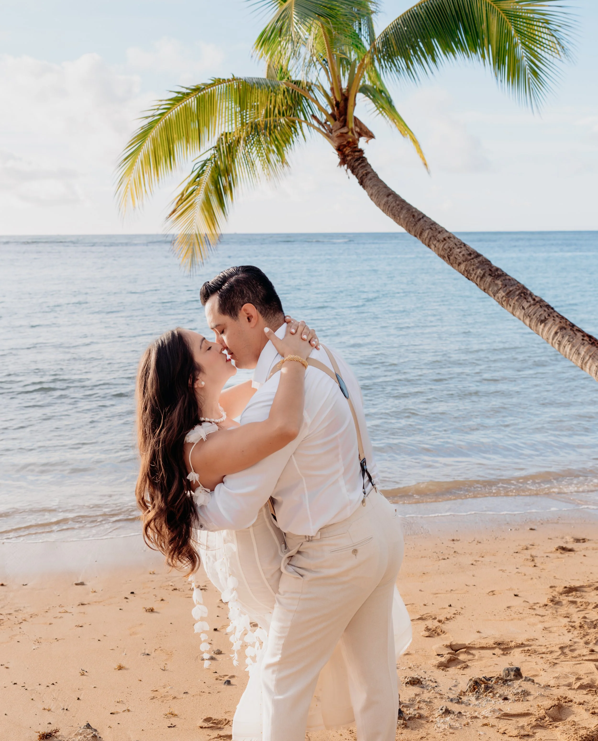 A couple dances on the beach under a palm tree, about to kiss, with the ocean in the background.