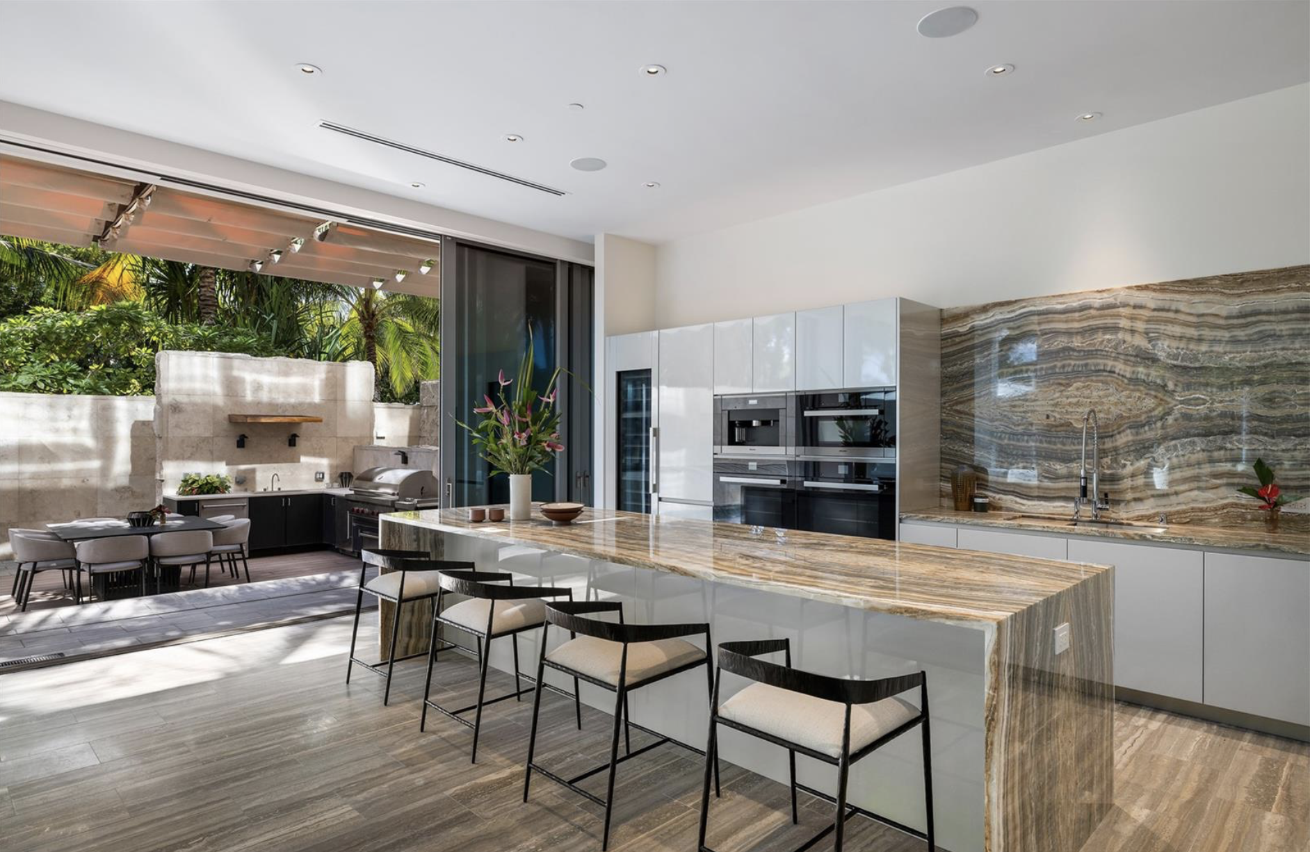 Modern kitchen with white cabinets, marble island, and outdoor dining area with a built-in grill and lush greenery outside.and premium architectural detail. Perfect for developers, agents, and designers.