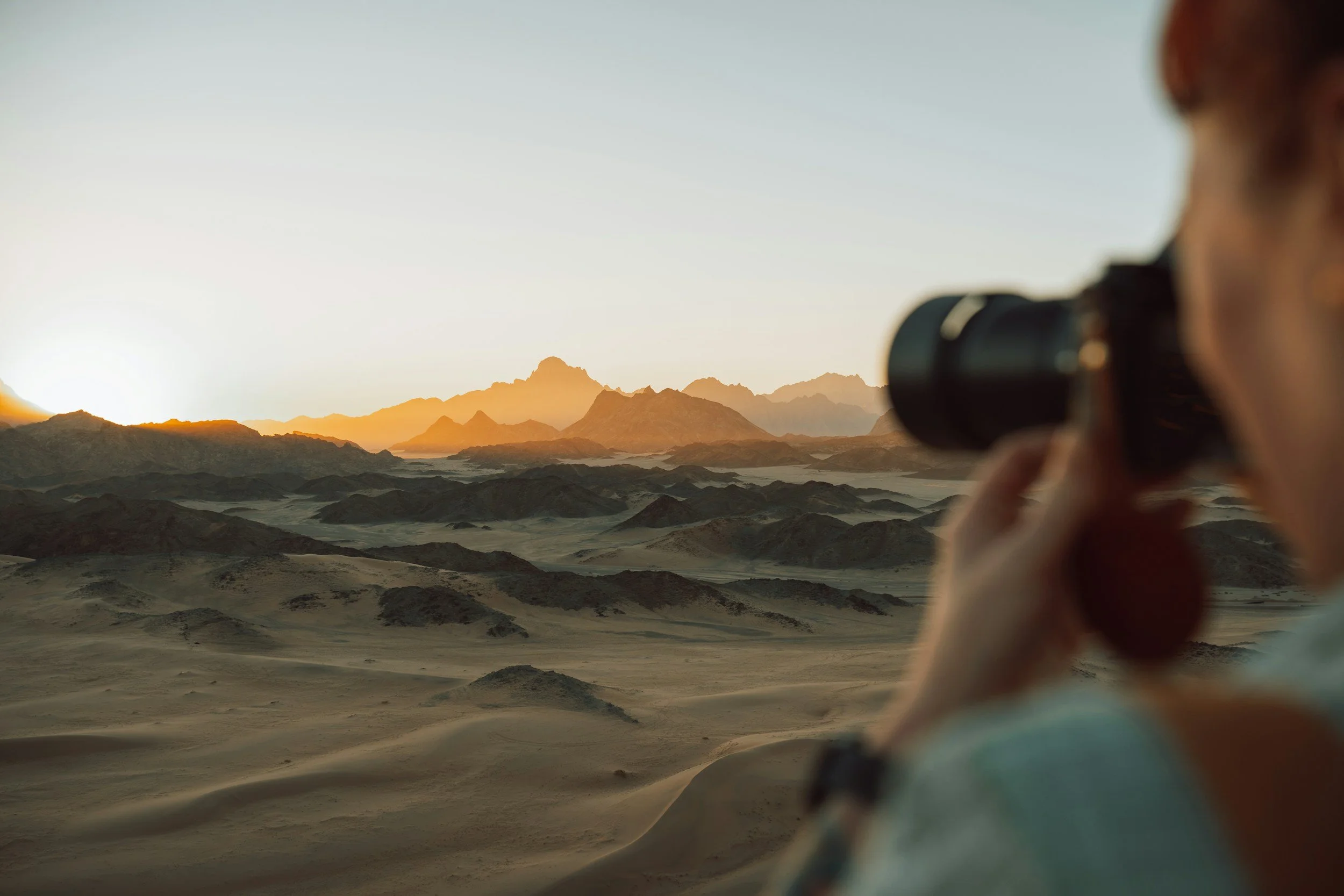 Person looking through binoculars at a desert landscape with mountains during sunset.