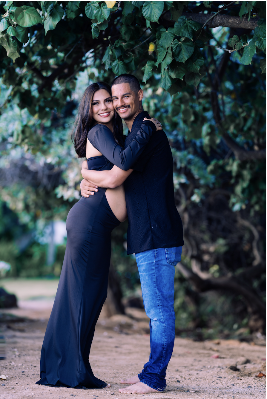 A smiling couple hugging with trees and greenery in the background.