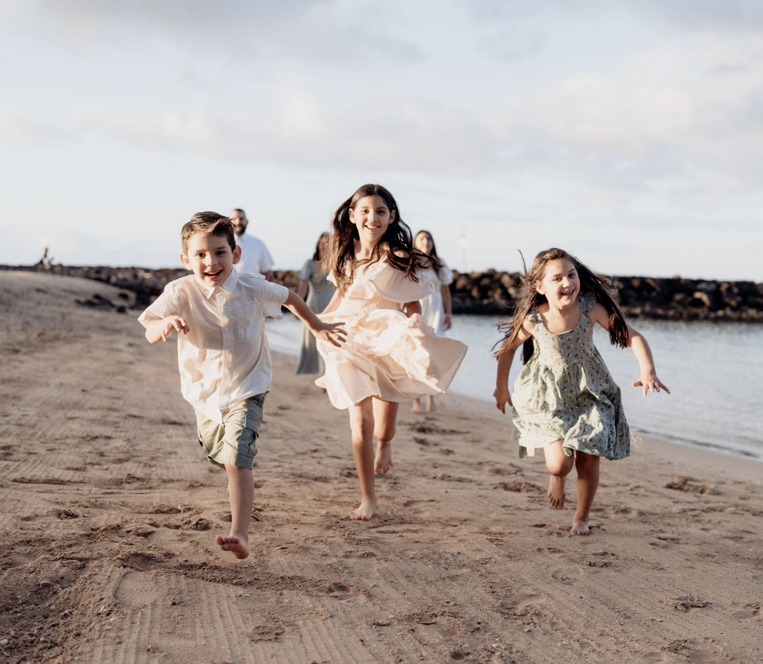 Children running on a sandy beach near the water, smiling and having fun during sunset.