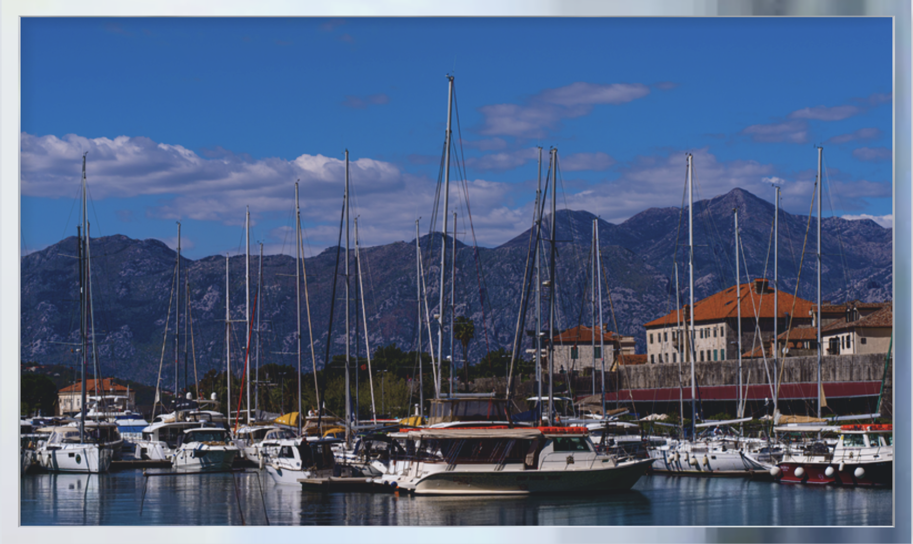 Sailboats and luxury yachts in a Mediterranean marina surrounded by dramatic mountains and coastal architecture, fine art photography print.