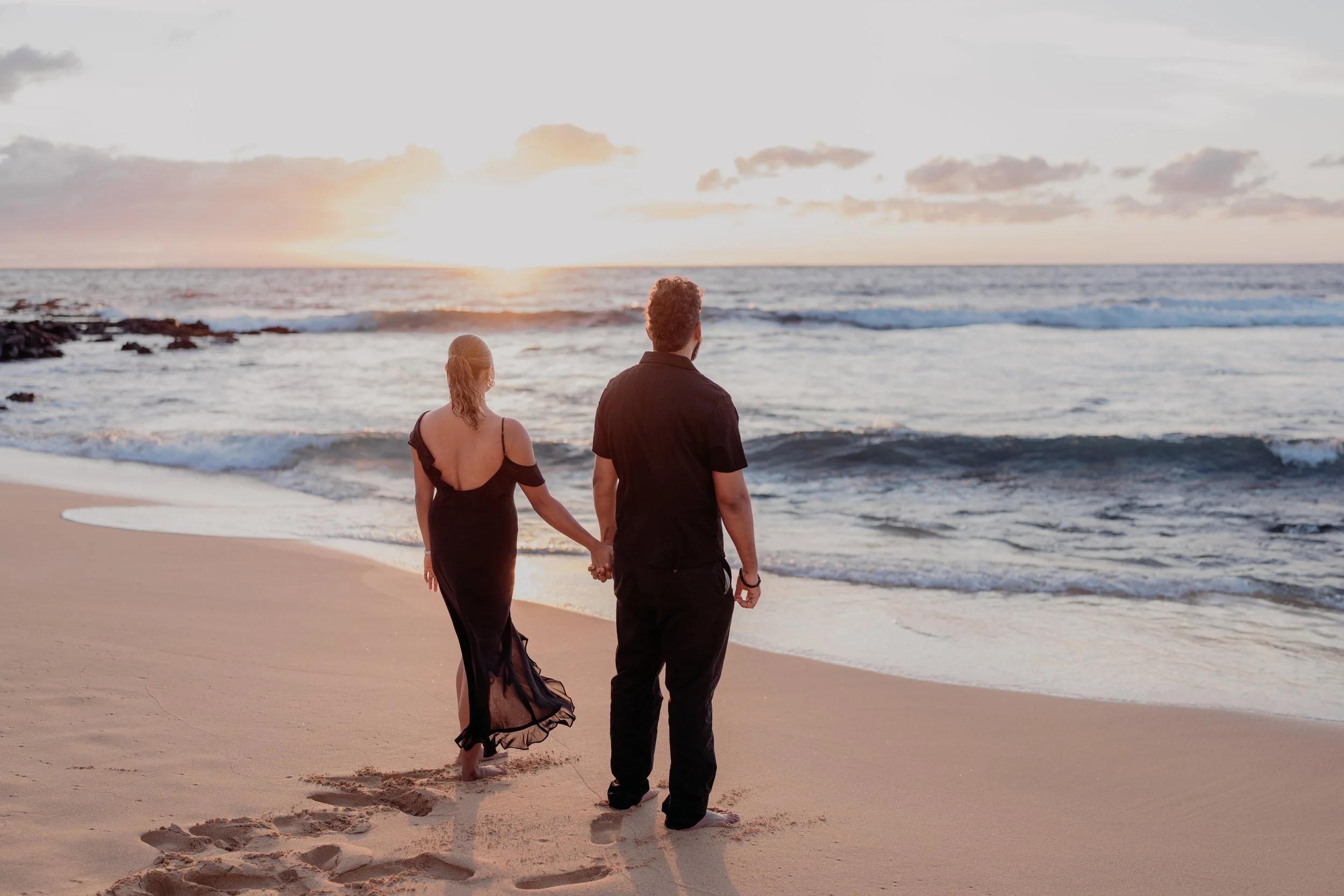A couple walking hand in hand on the beach during sunset.