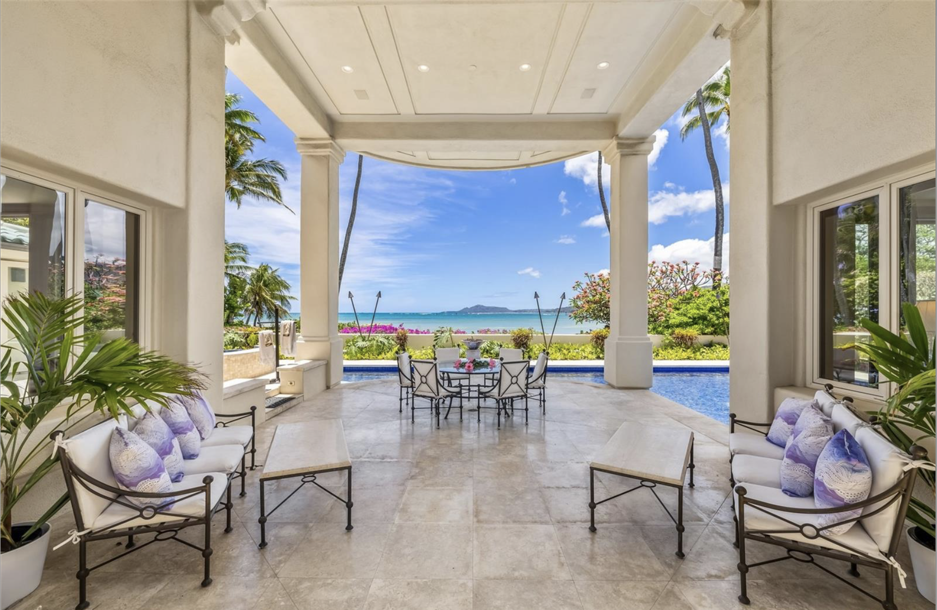 Elegant outdoor patio with seating, overlooking a tropical landscape with palm trees and a view of the ocean and distant islands.