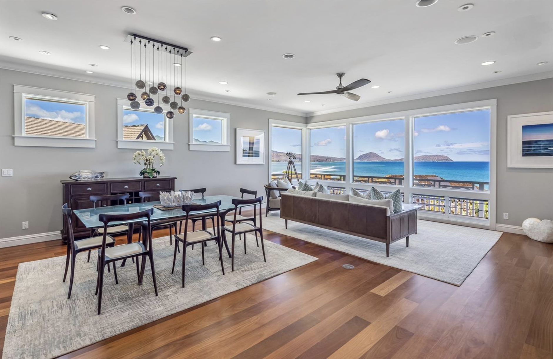 Living room with large windows overlooking the ocean, a dining table with chairs, a sofa, a sideboard, and decorative items.and premium architectural detail. Perfect for developers, agents, and designers.