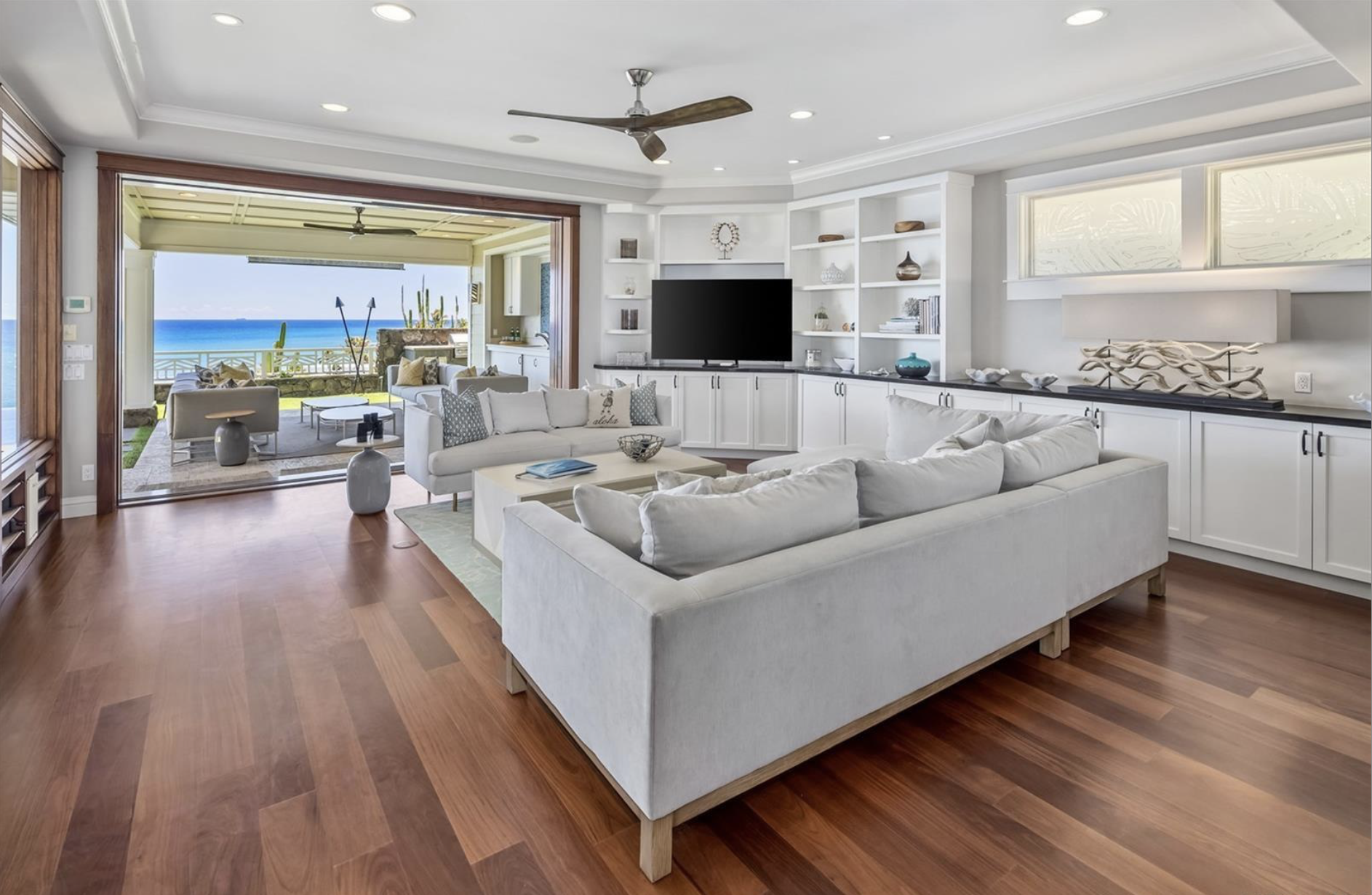 Living room with white sofas and a view of the ocean through sliding glass doors to a porch.