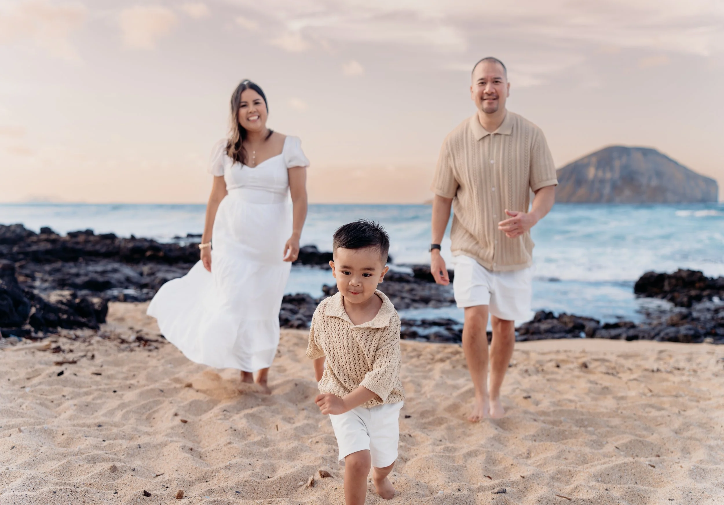 Family of four walking on a sandy beach with an ocean and a large island in the background during sunset or sunrise.