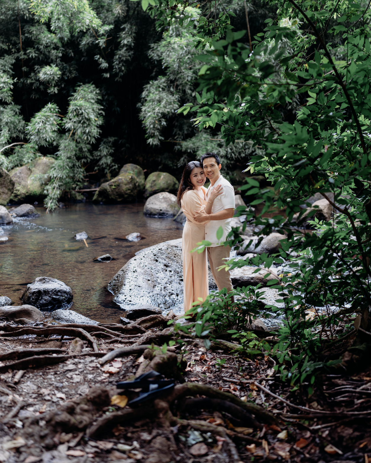 A couple embracing near a river in a lush green forest.