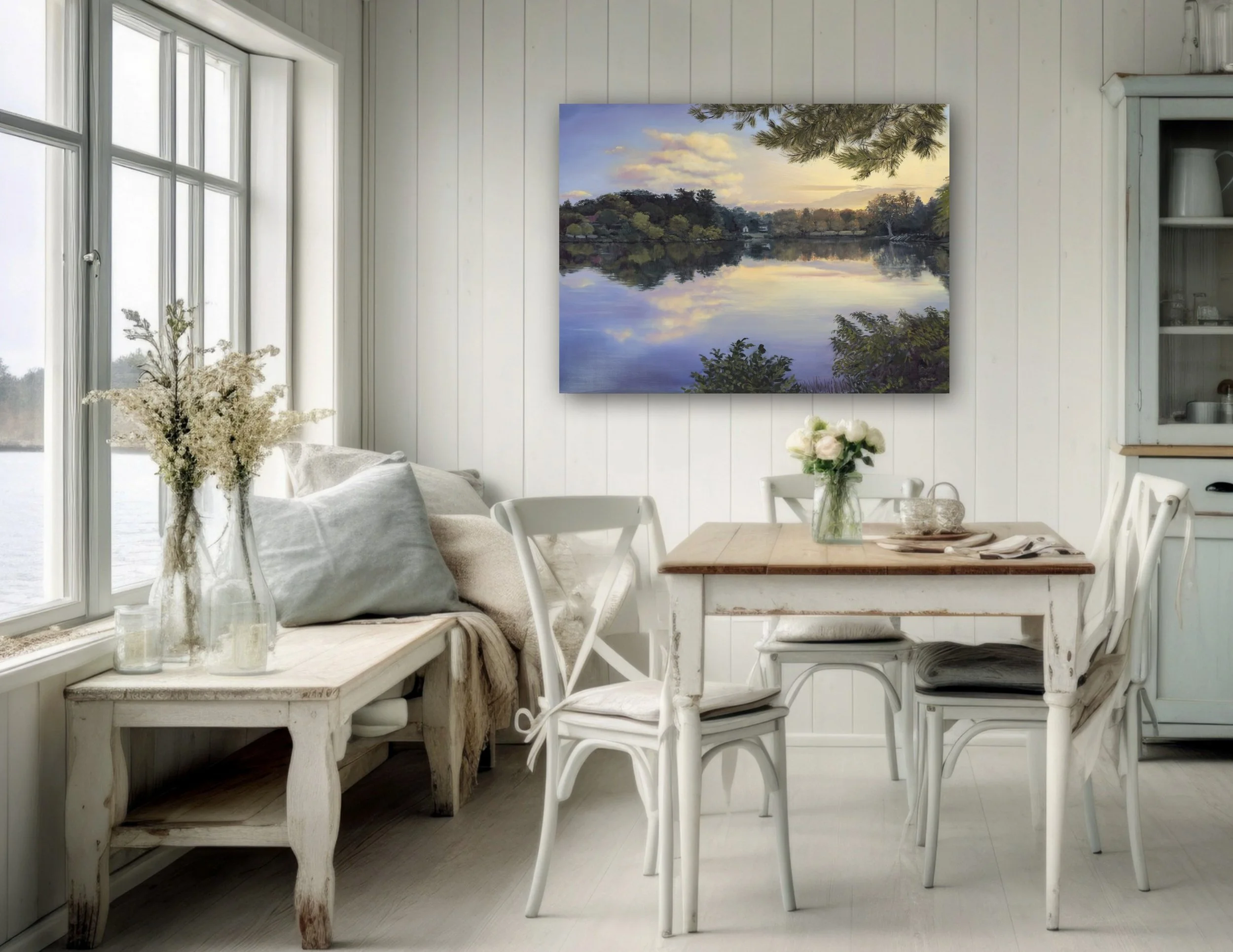 Cozy dining area with white walls and furniture, a large window with a view of water, a painting of a lake scene on the wall, and various vases and cushions for decoration.