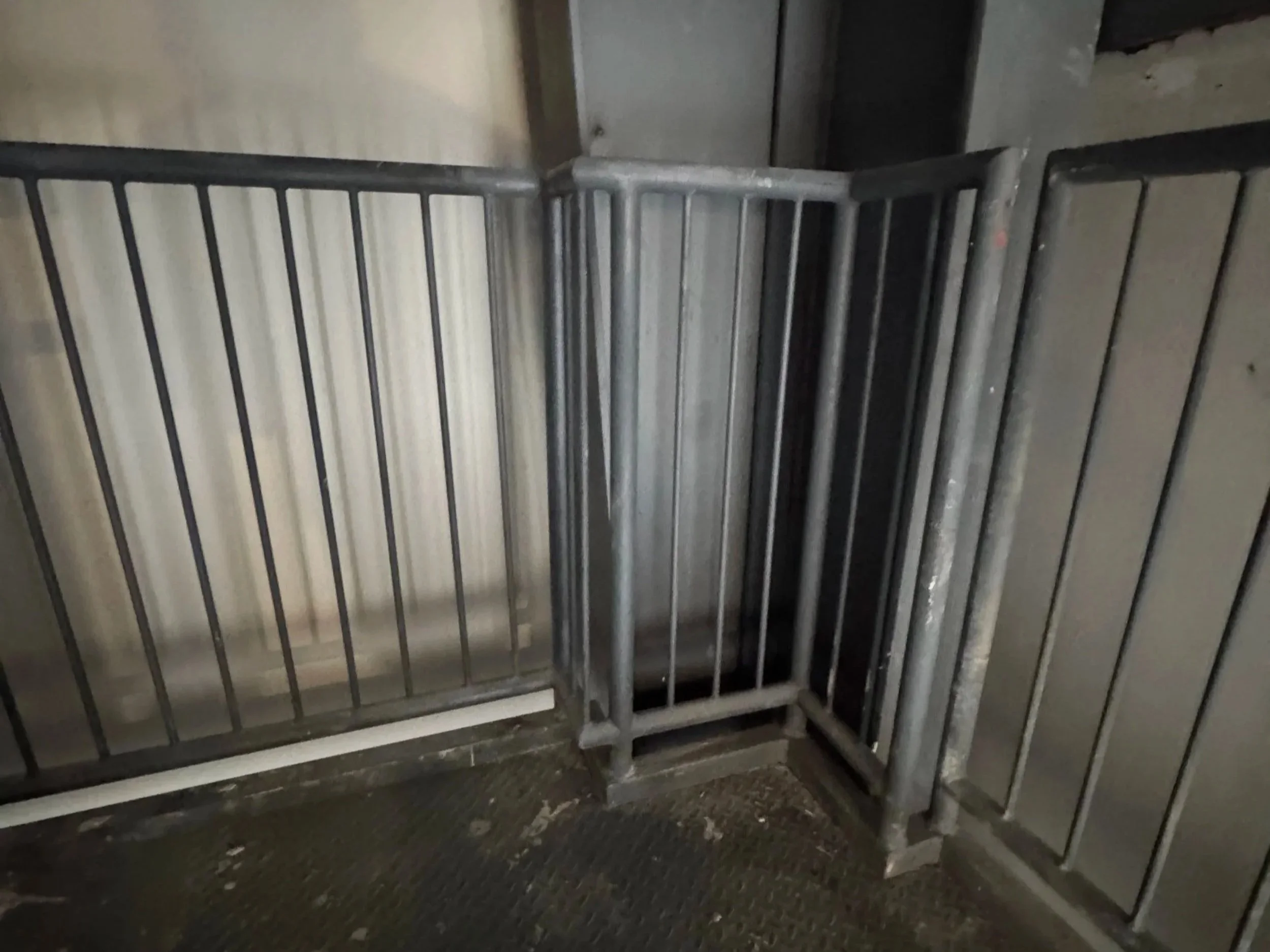 Metal gate or barrier in an industrial or commercial setting, with a black rubber mat on the floor.
